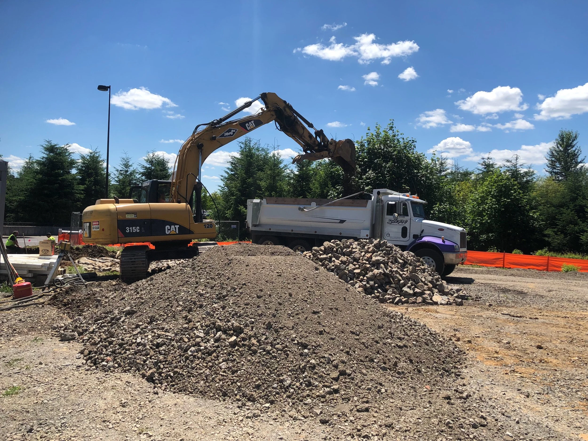 Construction site with a Caterpillar excavator loading rocks into a dump truck on a sunny day with blue sky and clouds.