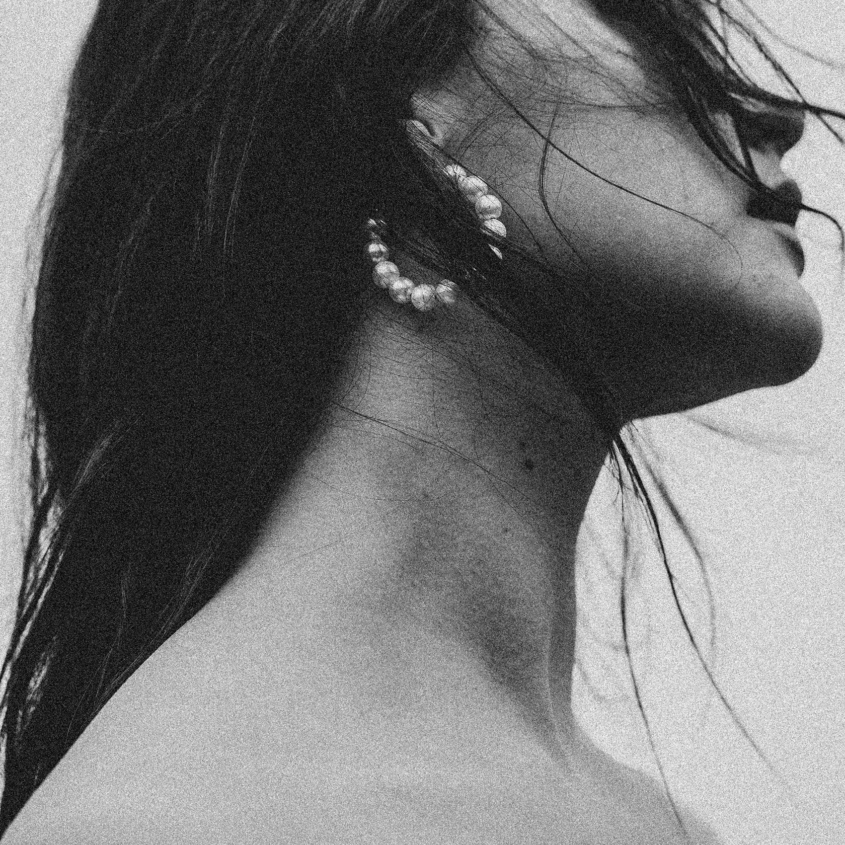 Close-up of a woman's profile in black and white, with wet hair, wearing pearl earrings, and shown from the neck up.