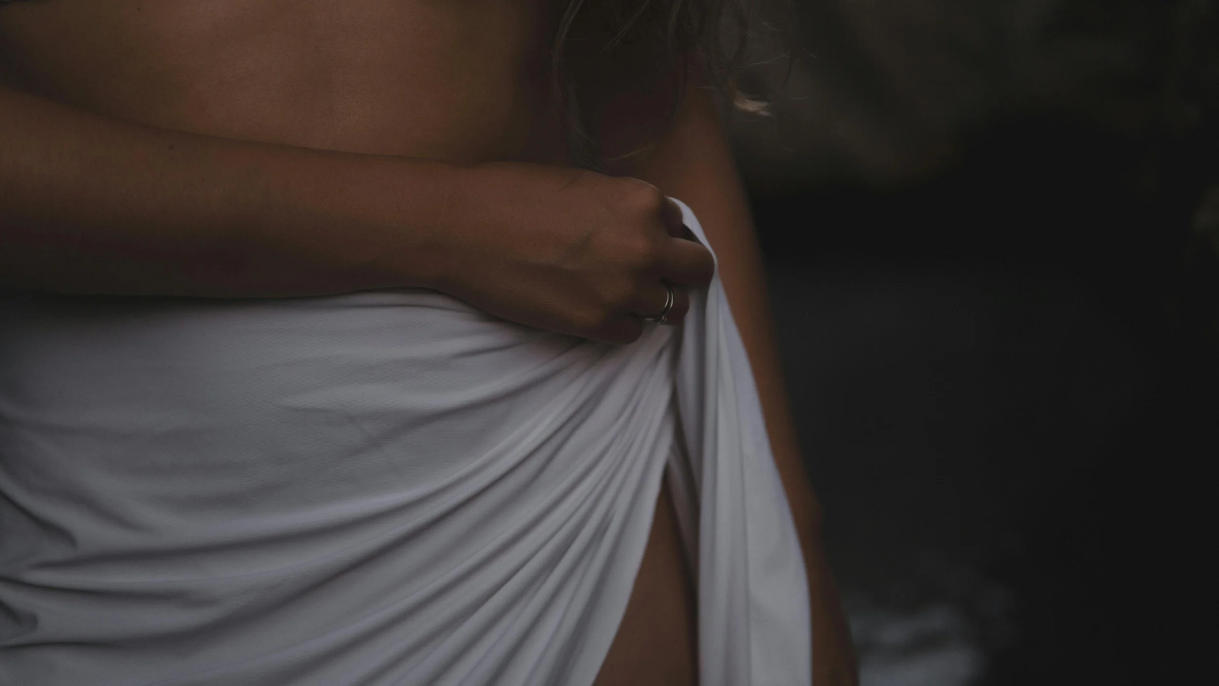 Close-up of a woman holding a white piece of cloth against her shoulder, with a dark background.