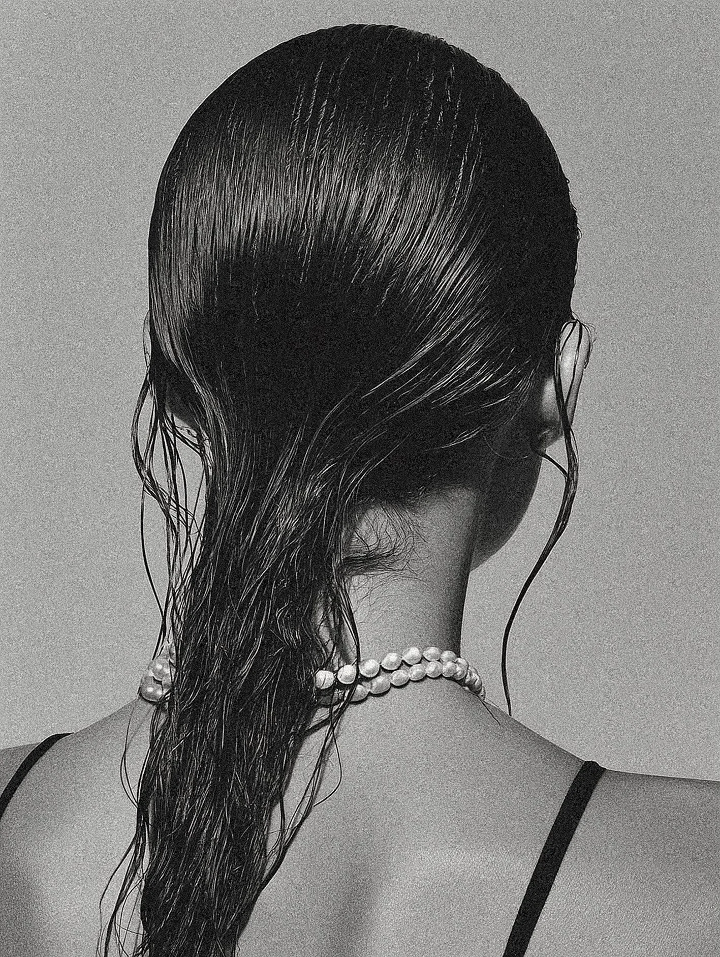 Back of a woman with wet hair, wearing a pearl necklace and a thin-strapped top.
