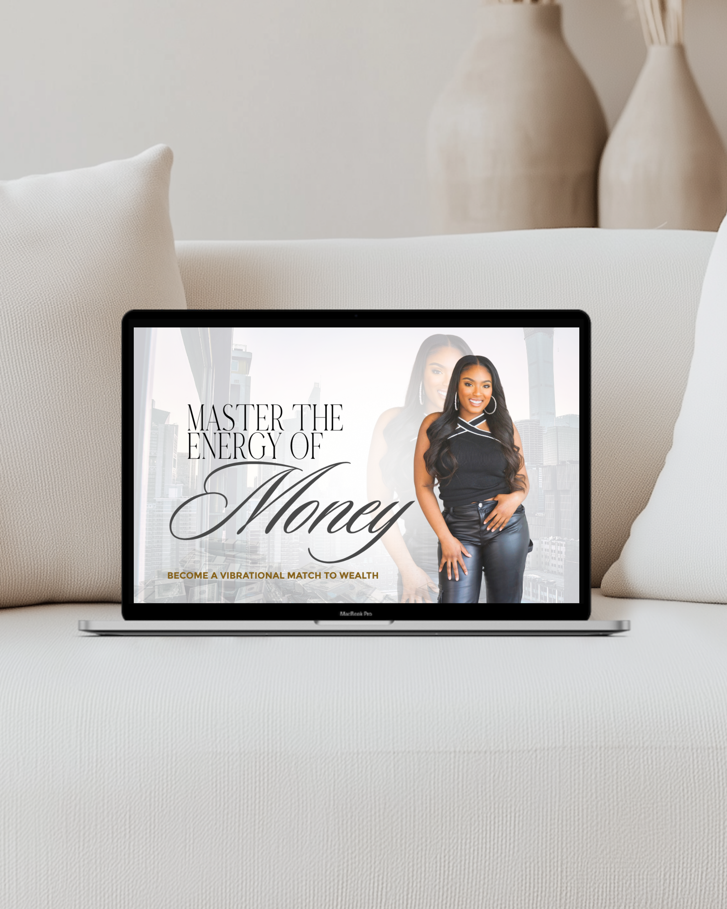 Laptop on a white sofa displaying a promotional image of a woman with long dark hair, wearing a black sleeveless top and leather pants. The text reads 'Master the Energy of Money' with a cityscape in the background.
