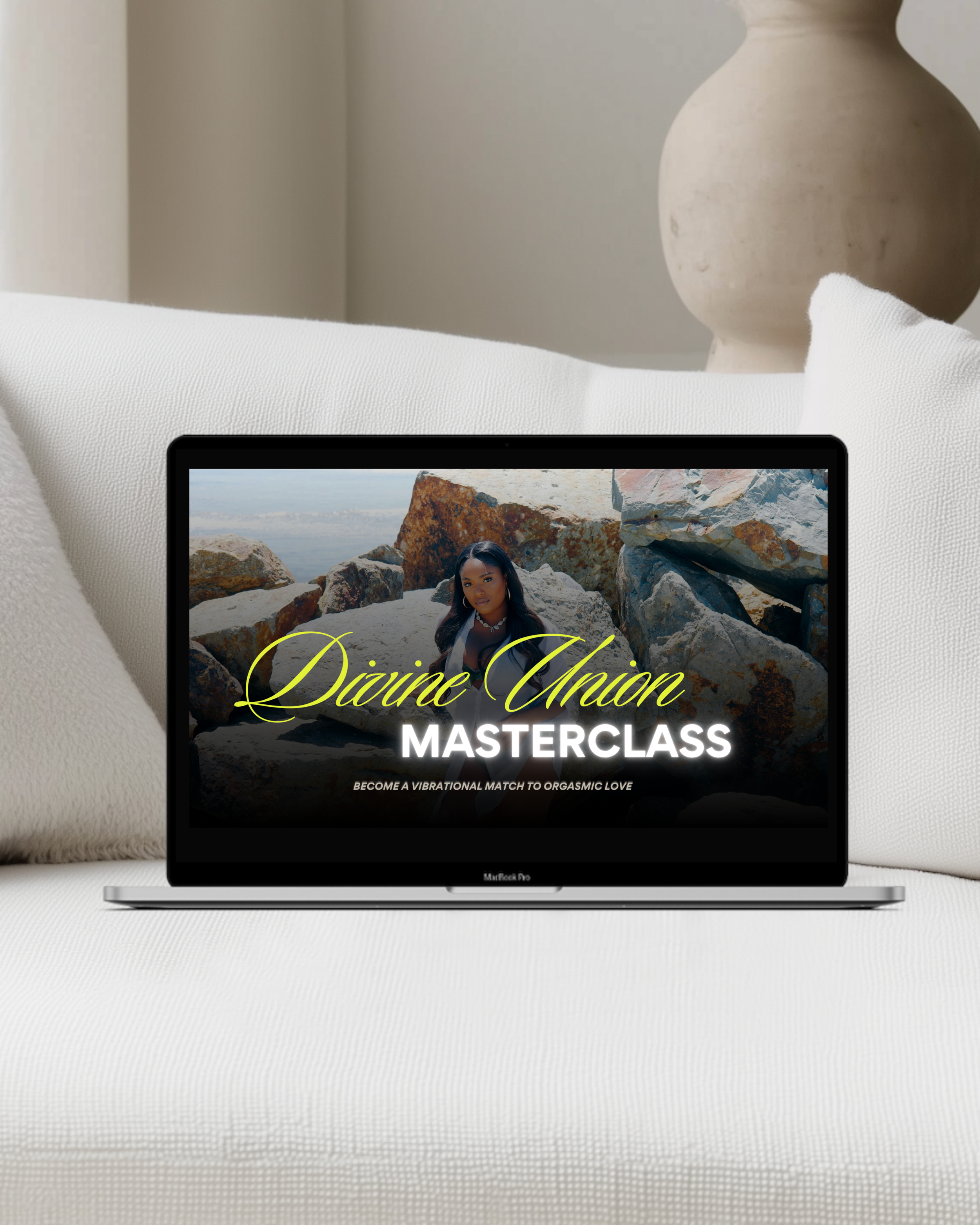 A laptop on a white couch screen displays an advertisement for a 'Divine Union Masterclass' with a woman among rocks and a landscape in the background.