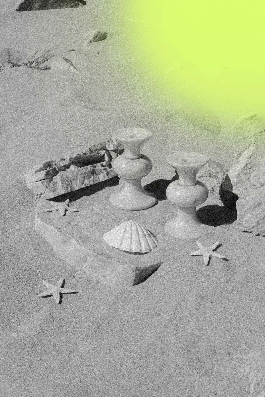 Beach scene with two ceramic candle holders, seashells, starfish, rocks, and sand.