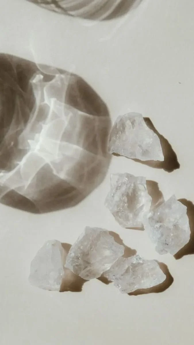 Six irregularly shaped clear ice chunks on a white surface with shadows cast beneath them.