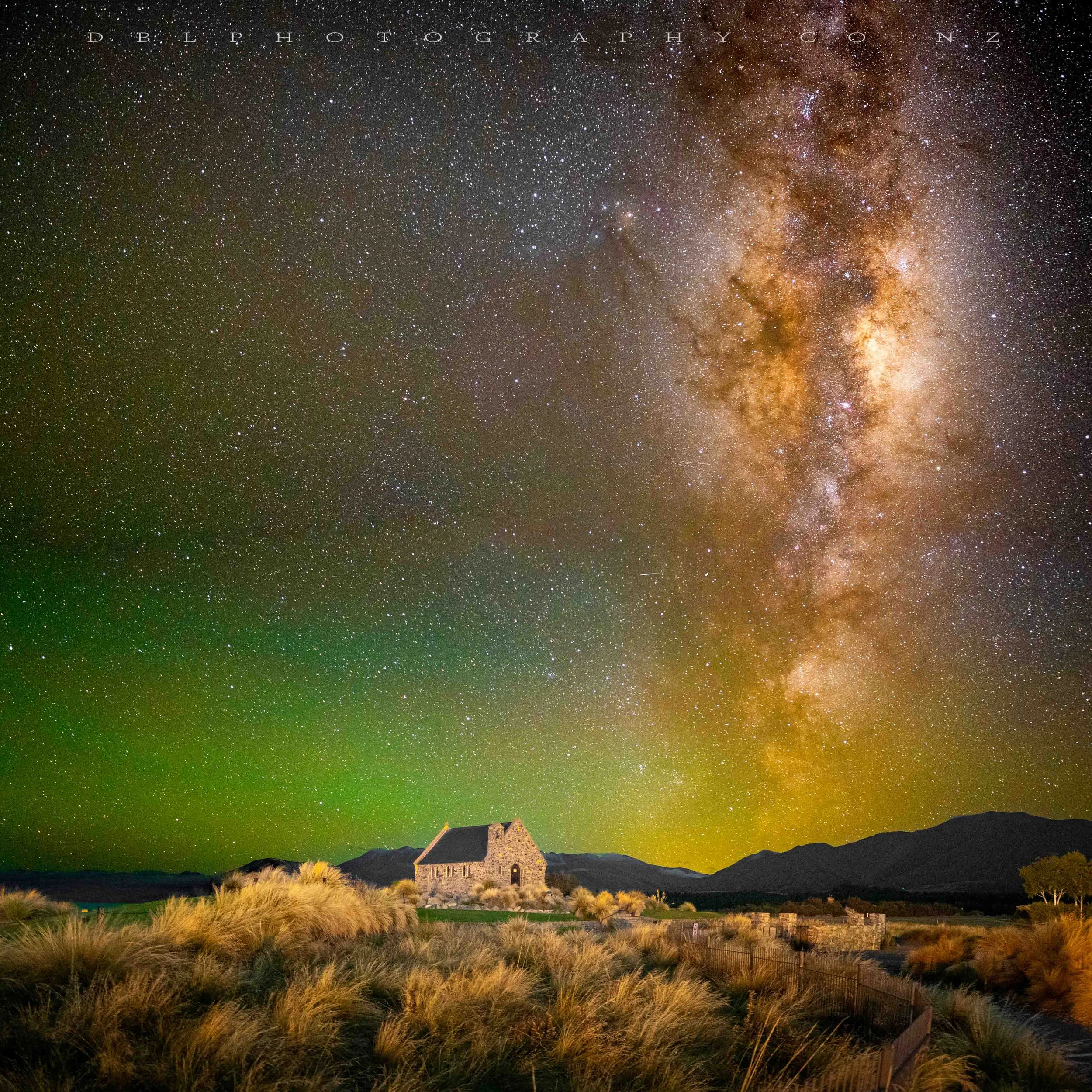 Nighttime landscape with a stone house among tall grass, mountains in the background, and a vibrant star-filled sky featuring the Milky Way galaxy.