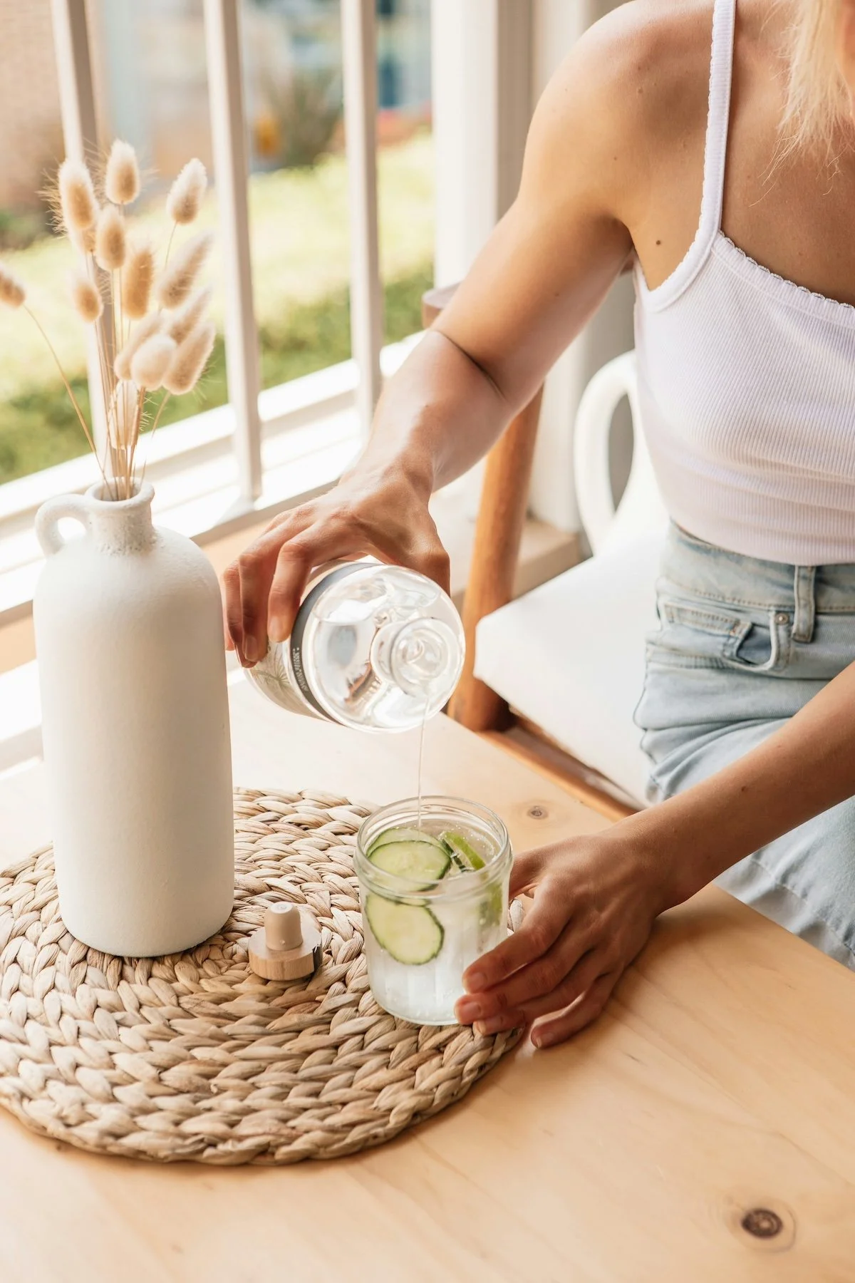 Pouring cucumber water near window with dried plants | simple hydration and seasonal wellness lifestyle image