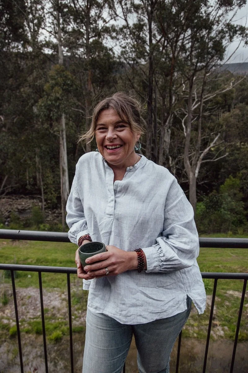 Kate Holman Naturopath smiling on balcony with trees holding mug | calm wellbeing lifestyle image for Simple Holistic Health