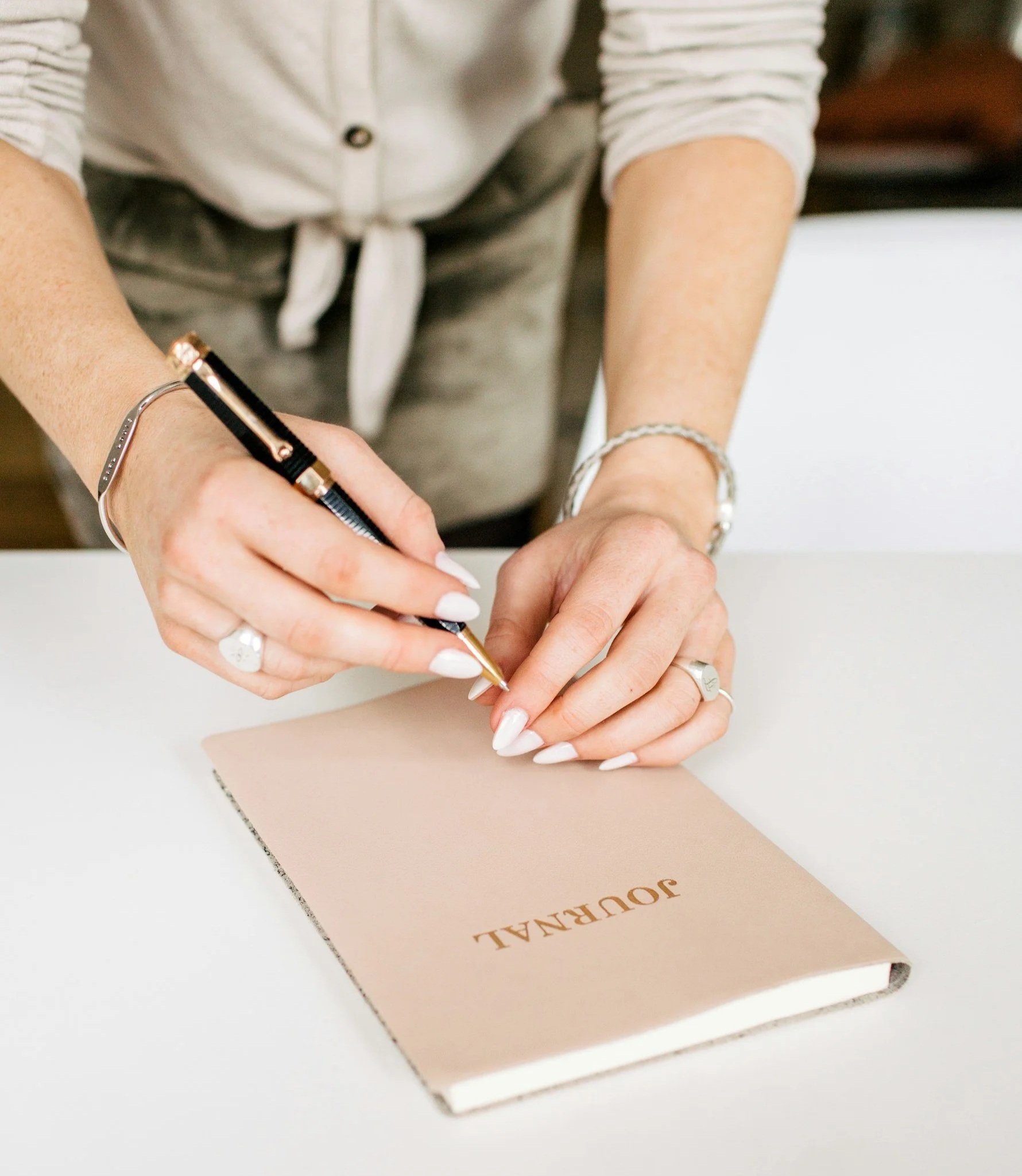 Person signing a guestbook titled 'JOURNAL' with a black pen on a white table.