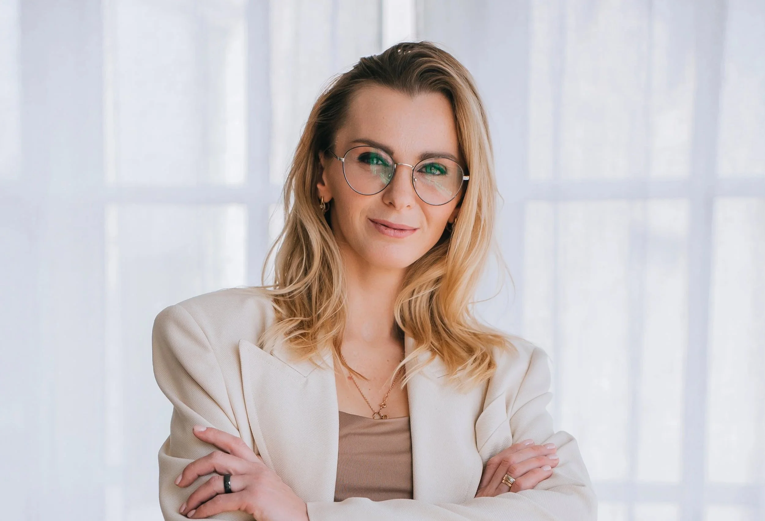 Portrait of a woman with blonde hair, wearing glasses and a cream-colored blazer, smiling confidently.