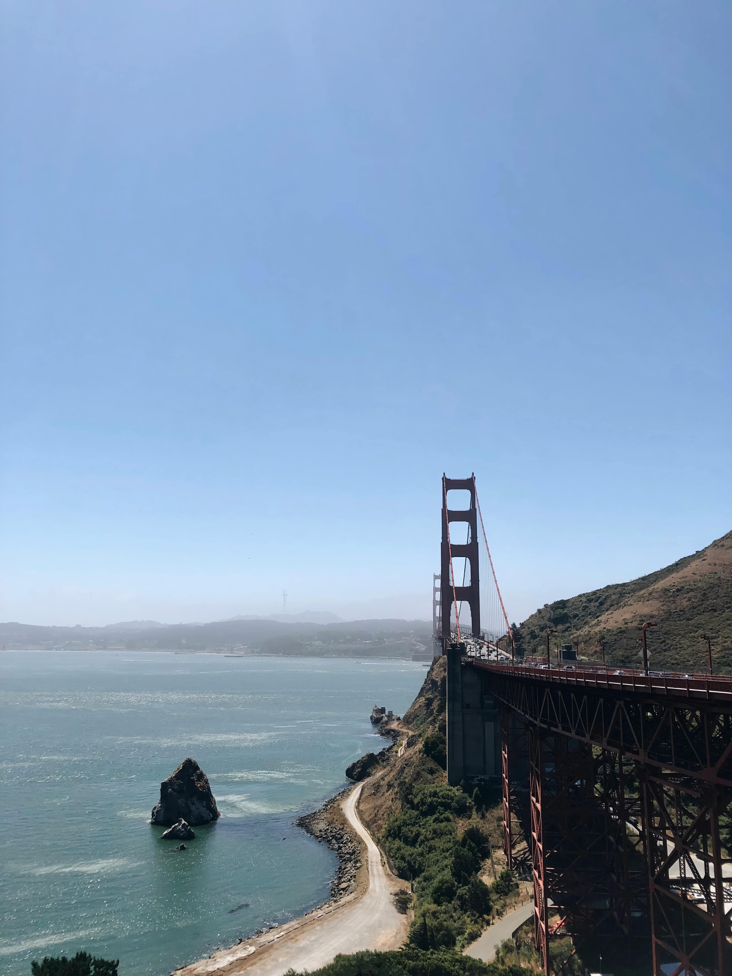 View of the Golden Gate Bridge in San Francisco, with the water and rocky shore in the foreground and hills in the background.