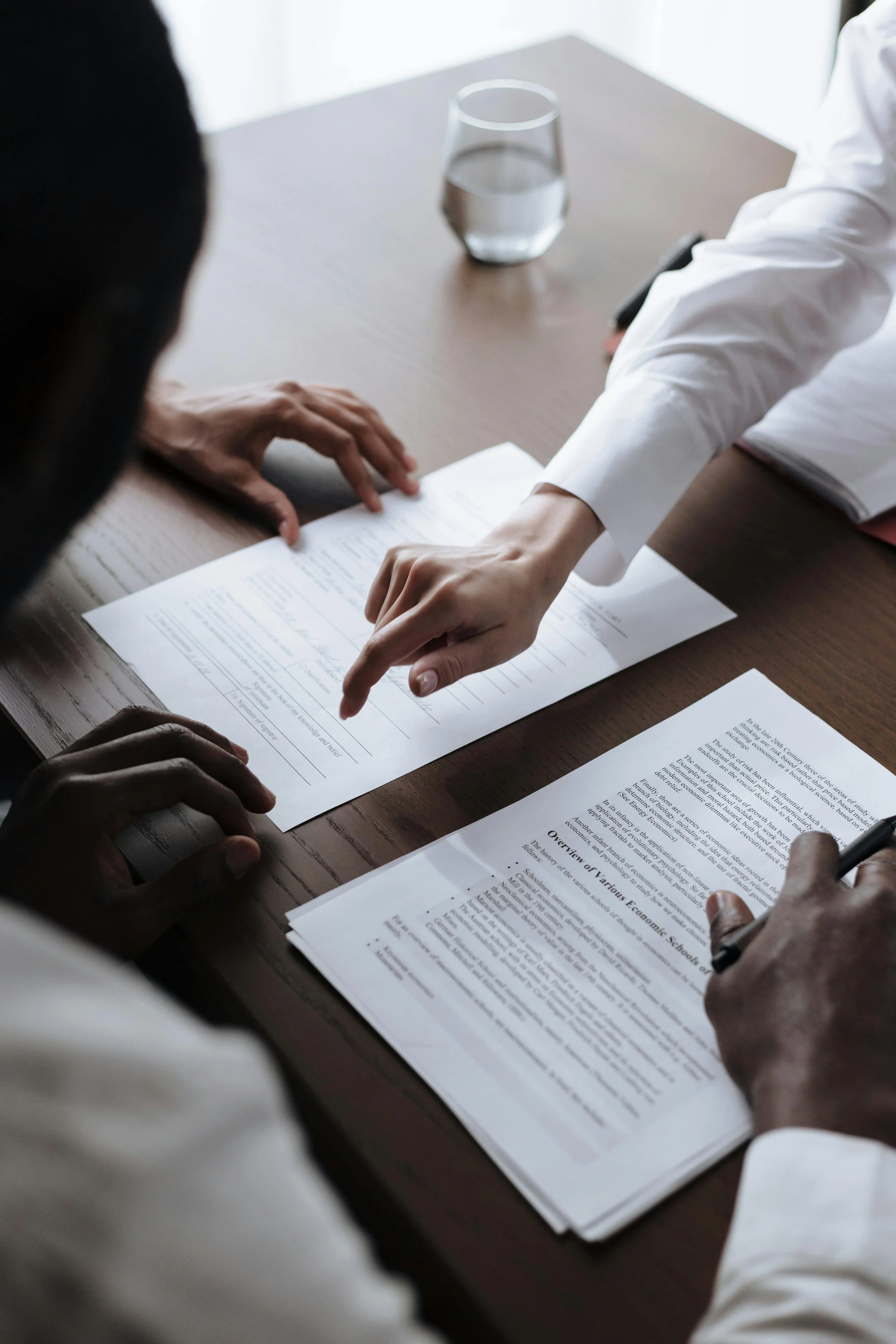 Two people reviewing documents on a wooden table, with a glass of water nearby.