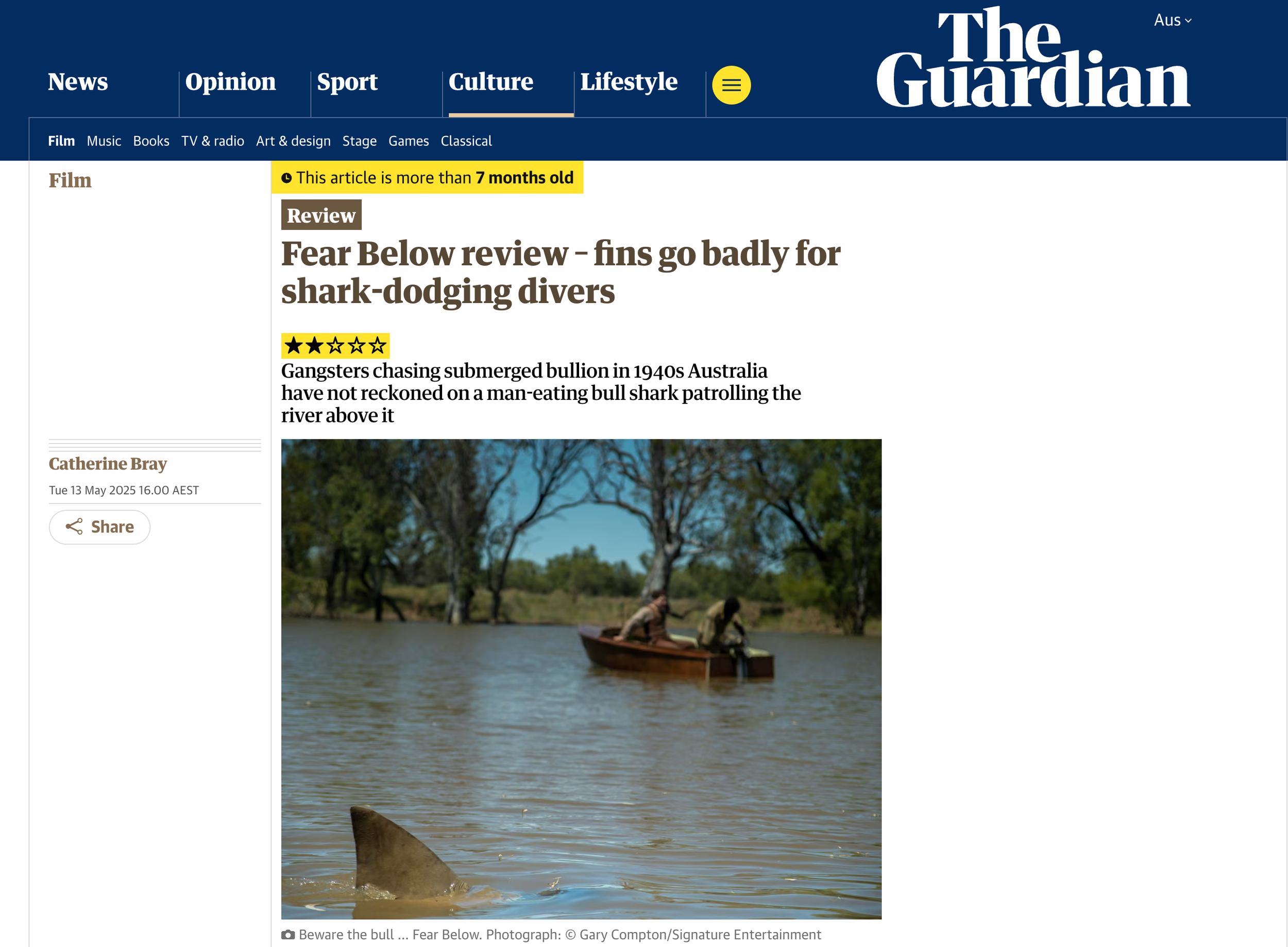 A boat with two people on a river, with trees on the riverbank and a submerged bull shark fin visible in the water in the foreground.
