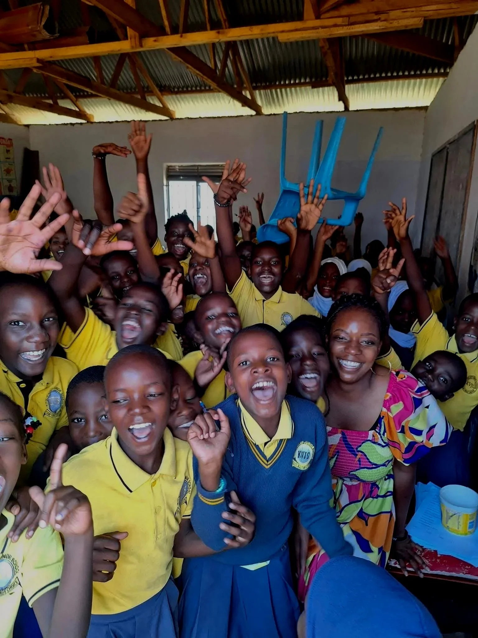 Group of smiling children and a woman in colorful dress celebrating inside a room with wooden ceiling beams