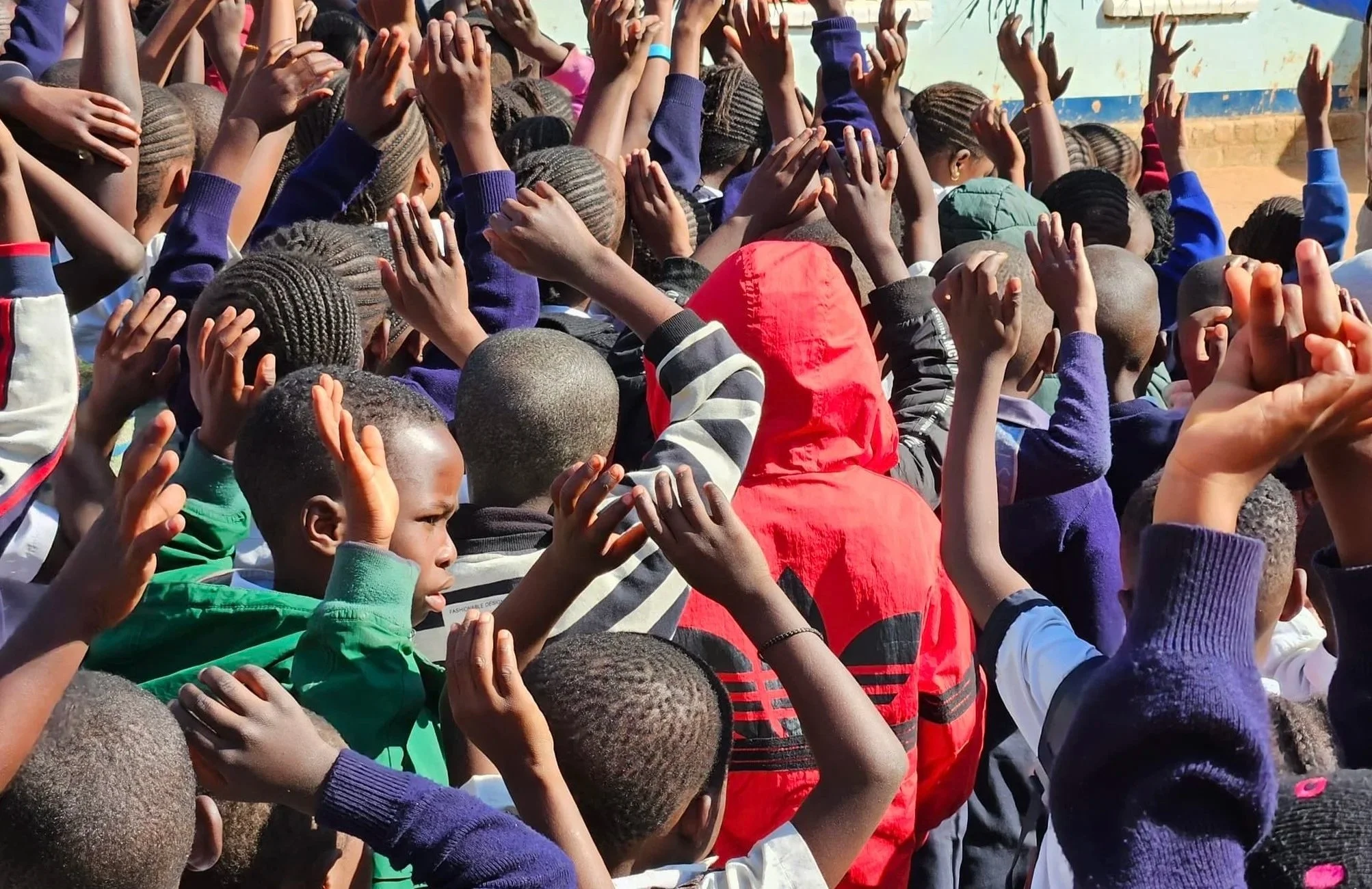 A large group of children with modern hairstyles raising their hands.