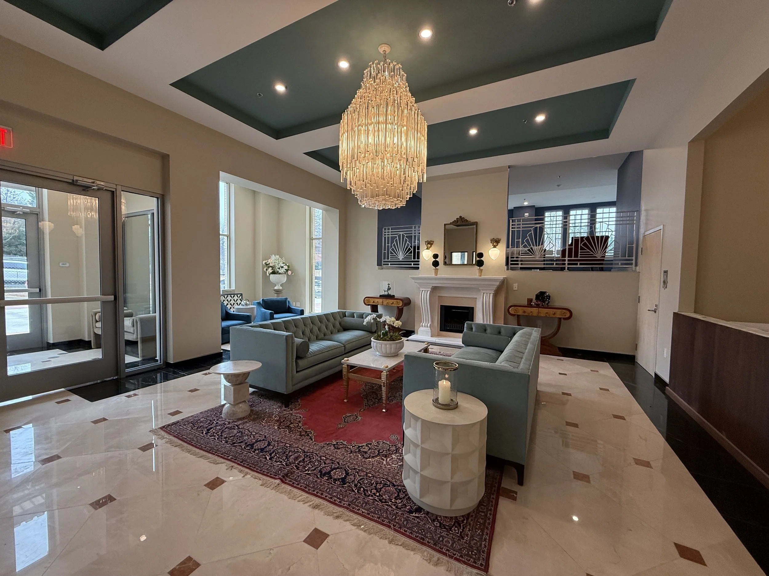 Elegant hotel lobby with high ceiling, grand chandelier, fireplace, plush sofas, and large windows letting in natural light.