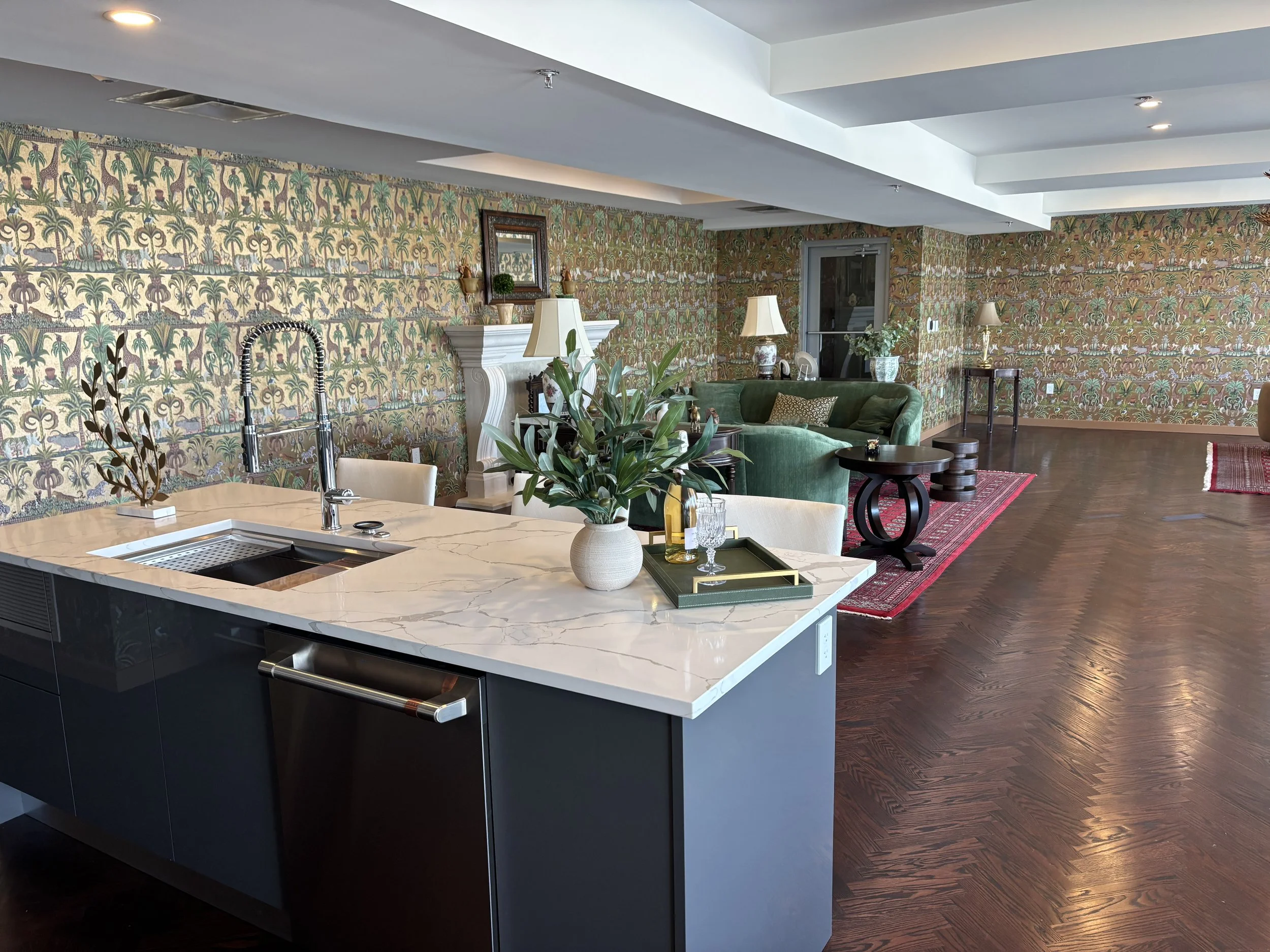 Open-concept living space with marble kitchen island, green sofa, patterned wallpaper, and hardwood floors.