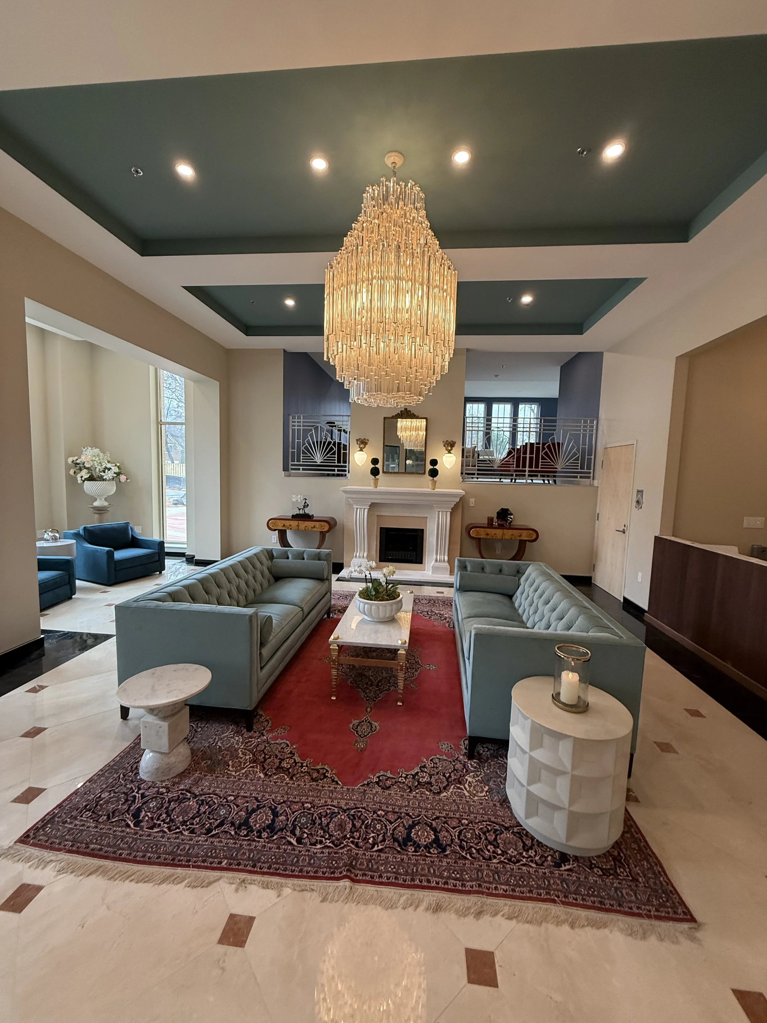 Elegant lobby with a large chandelier, mint green sofas, a fireplace, and decorative accents.