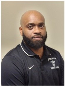 Headshot of a man with a beard and bald head wearing a black Nike polo shirt with white accents and a logo.