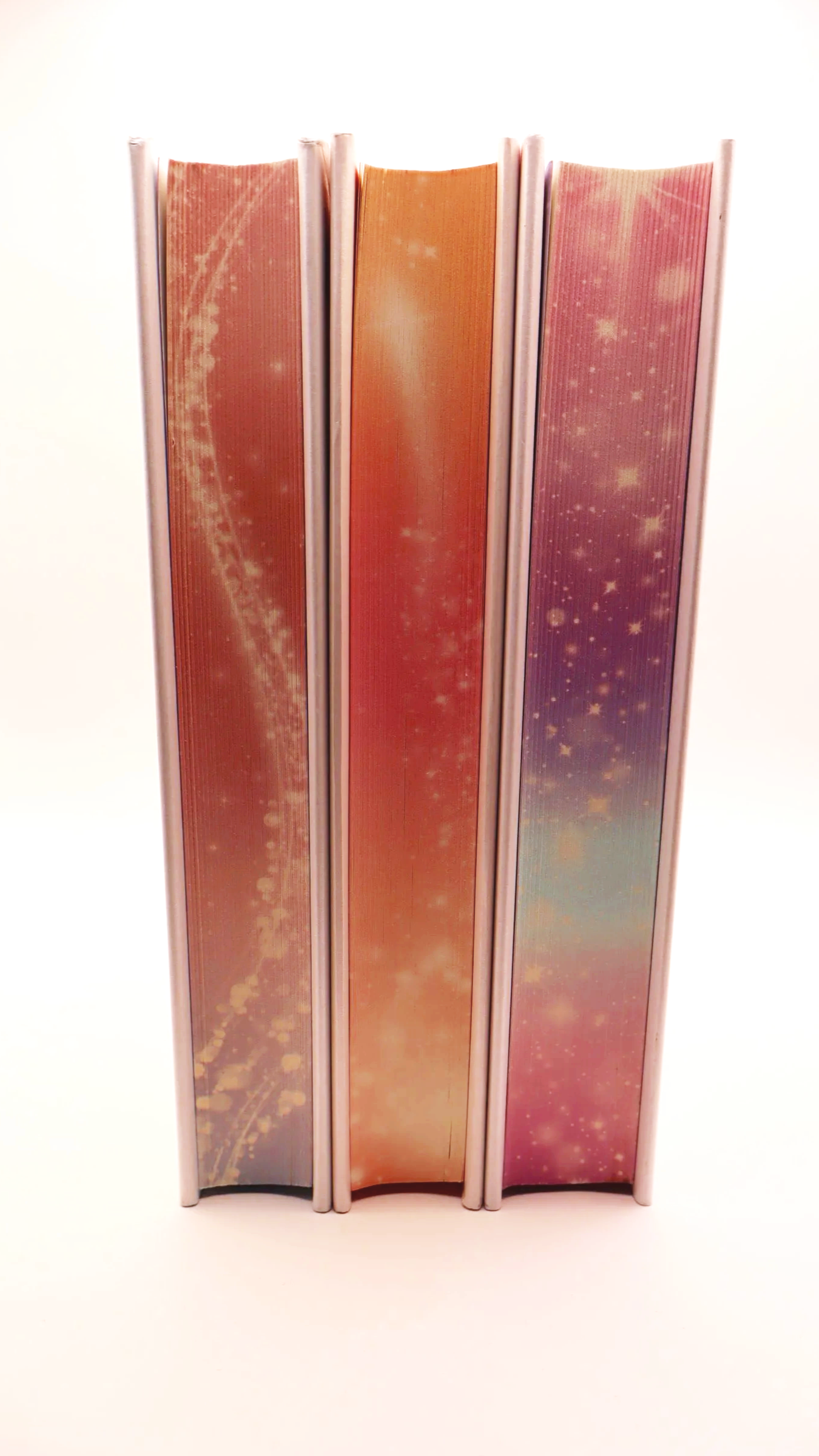 Vertical view of three books showing colorful, patterned sprayed edges with stars and swirls.