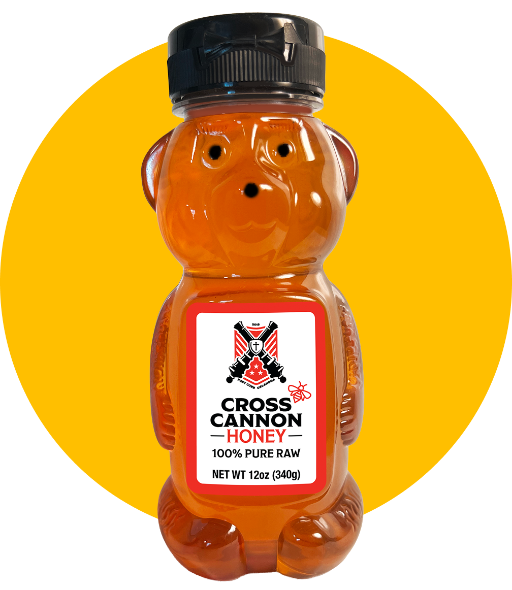 A bear-shaped bottle of Cross Cannon Honey with a black cap and a label indicating it contains 100% pure raw honey, weighing 12 ounces, set against a two-toned yellow and black background.