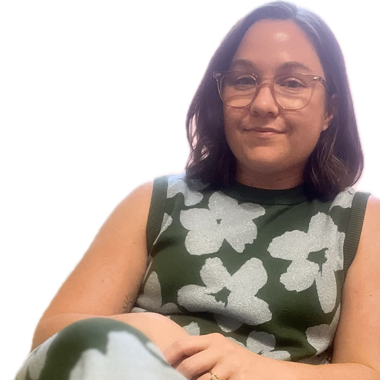 A woman with shoulder-length dark hair, wearing glasses and a sleeveless top with a silver floral pattern, smiling and sitting with her arms crossed.