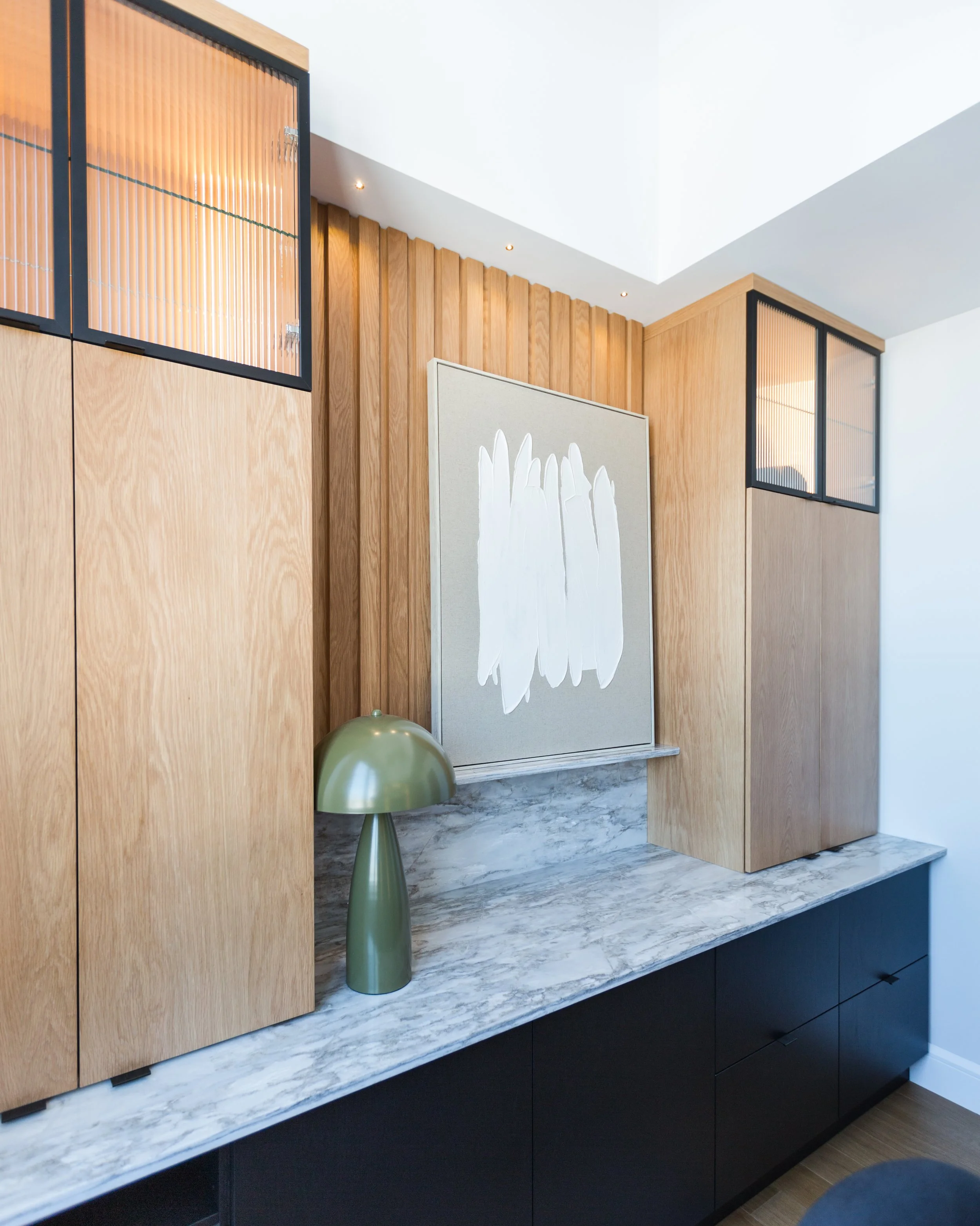 Modern interior with wooden cabinets, marble countertop, green table lamp, abstract white artwork, and black accents.