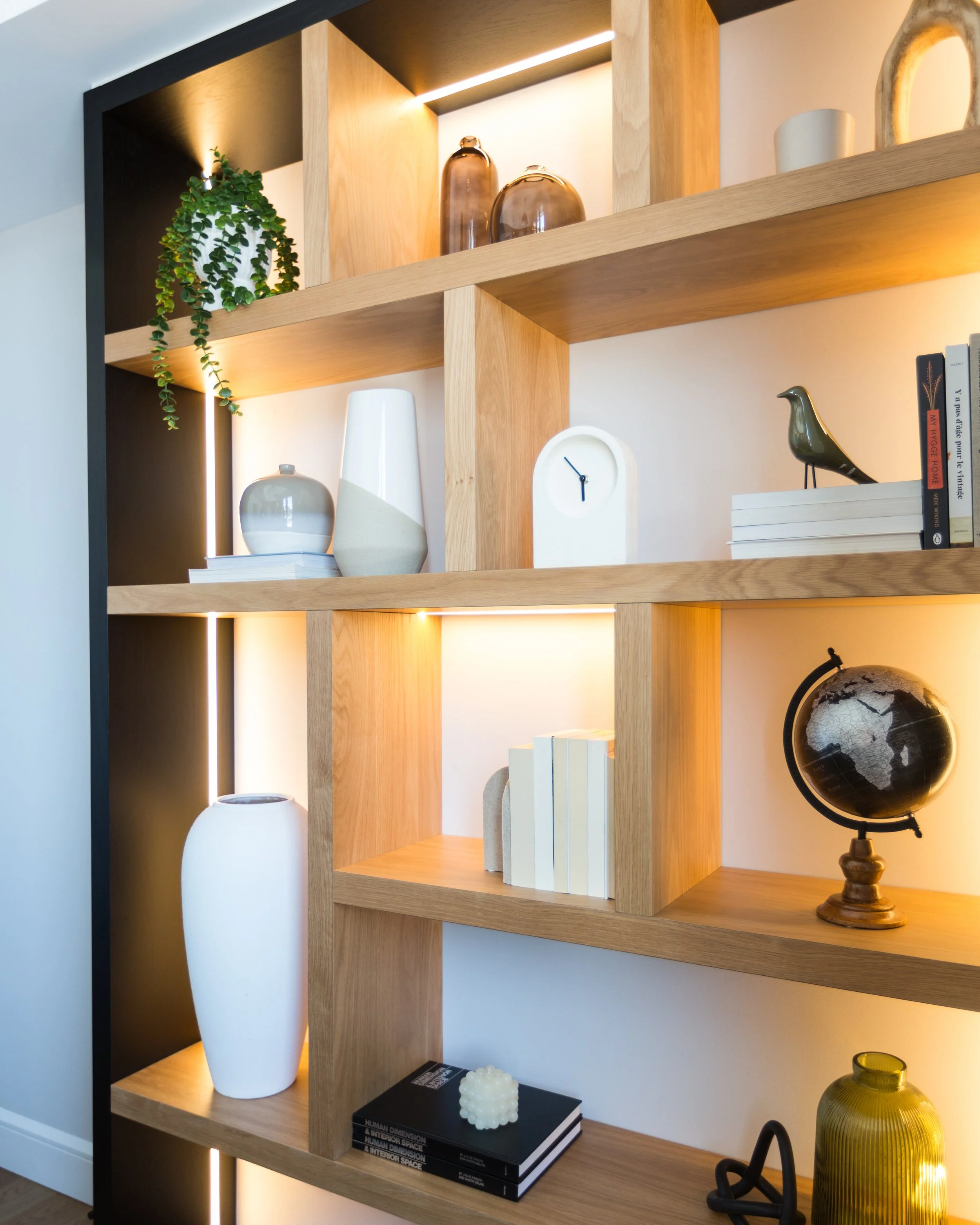 Wooden bookshelf with decorative items including vases, books, a globe, a clock, and a plant, with integrated lighting.