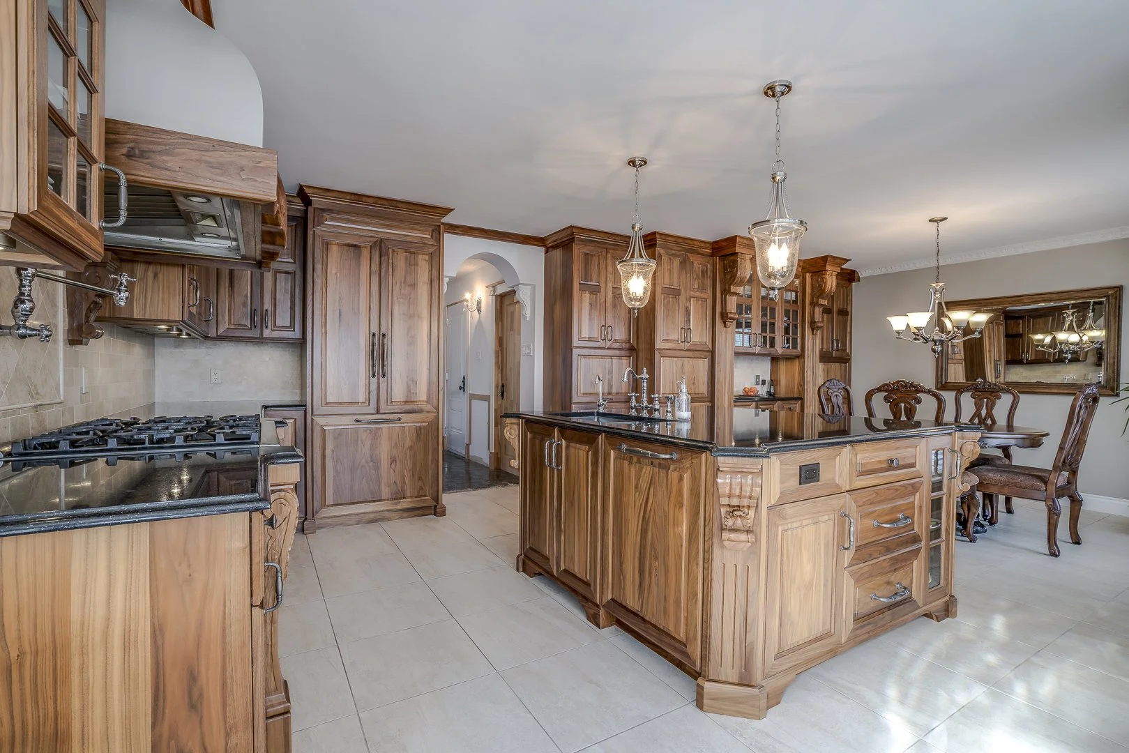 Kitchen with wooden cabinets, black countertop island, and chandelier, dining area with wooden table and chairs, mirror on wall.