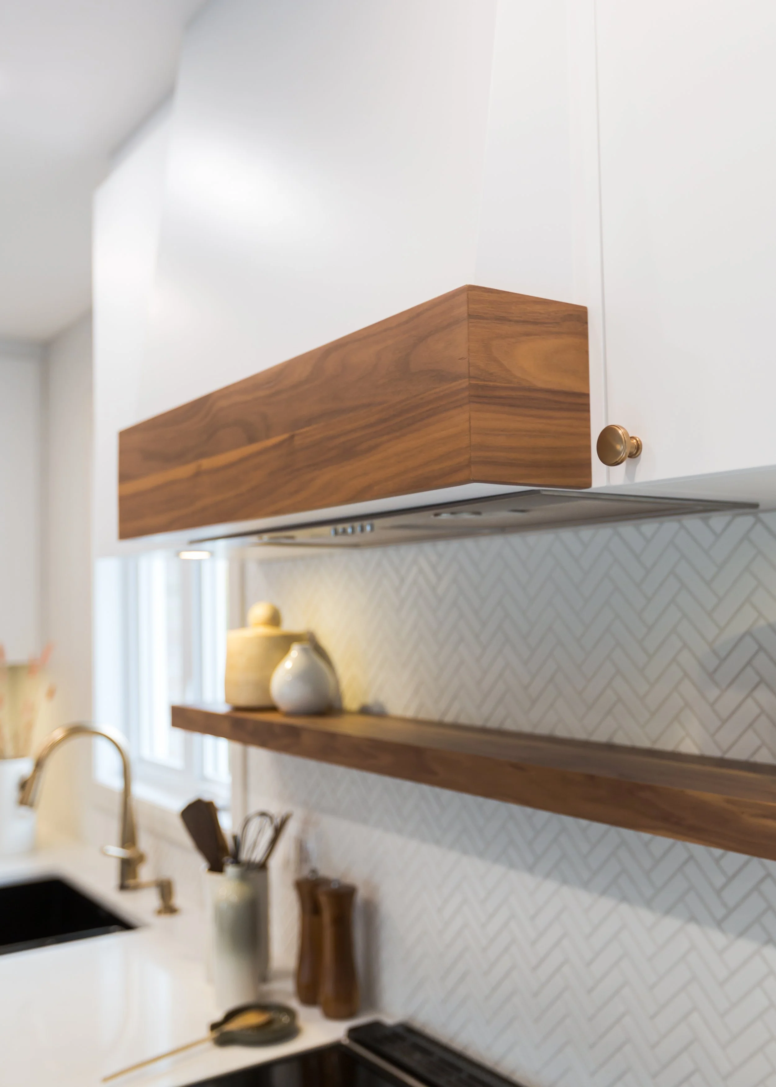 Close-up of a modern kitchen upper cabinet with a wood finish and white cabinetry, above a countertop with decorative vases and kitchen utensils.