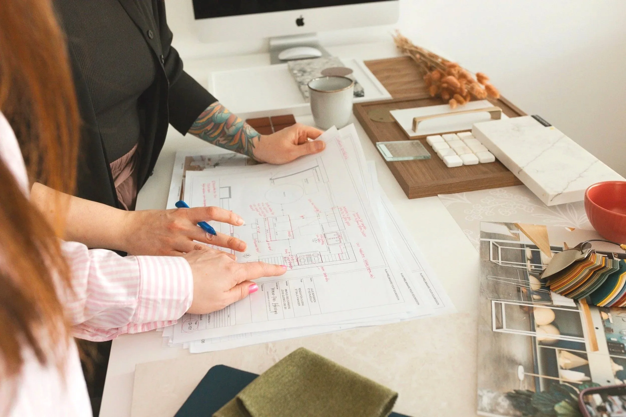 Two people reviewing architectural blueprints on a desk with color swatches, samples, and design materials.