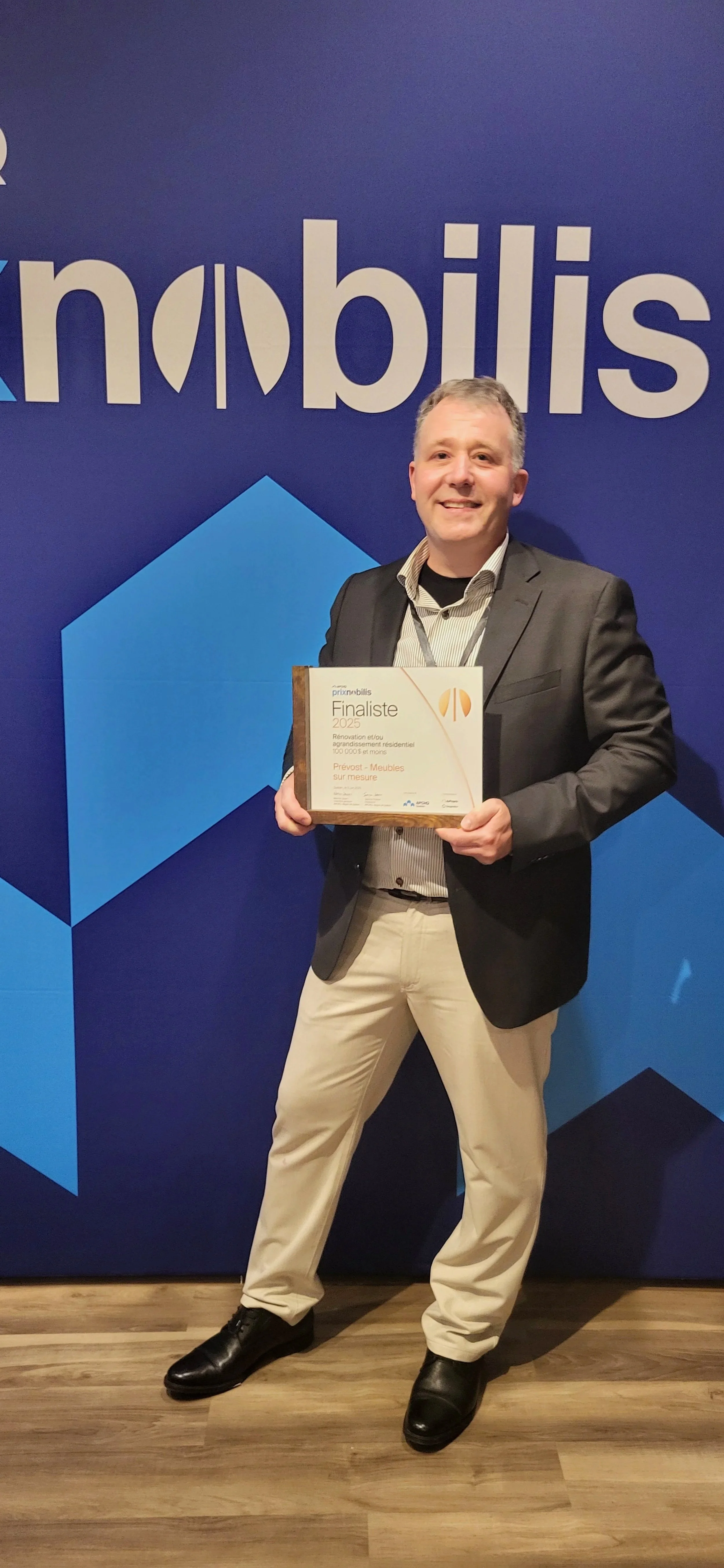 A man in a suit holding an award plaque, standing in front of a blue background with the word 'Prix Nobilis' visible.