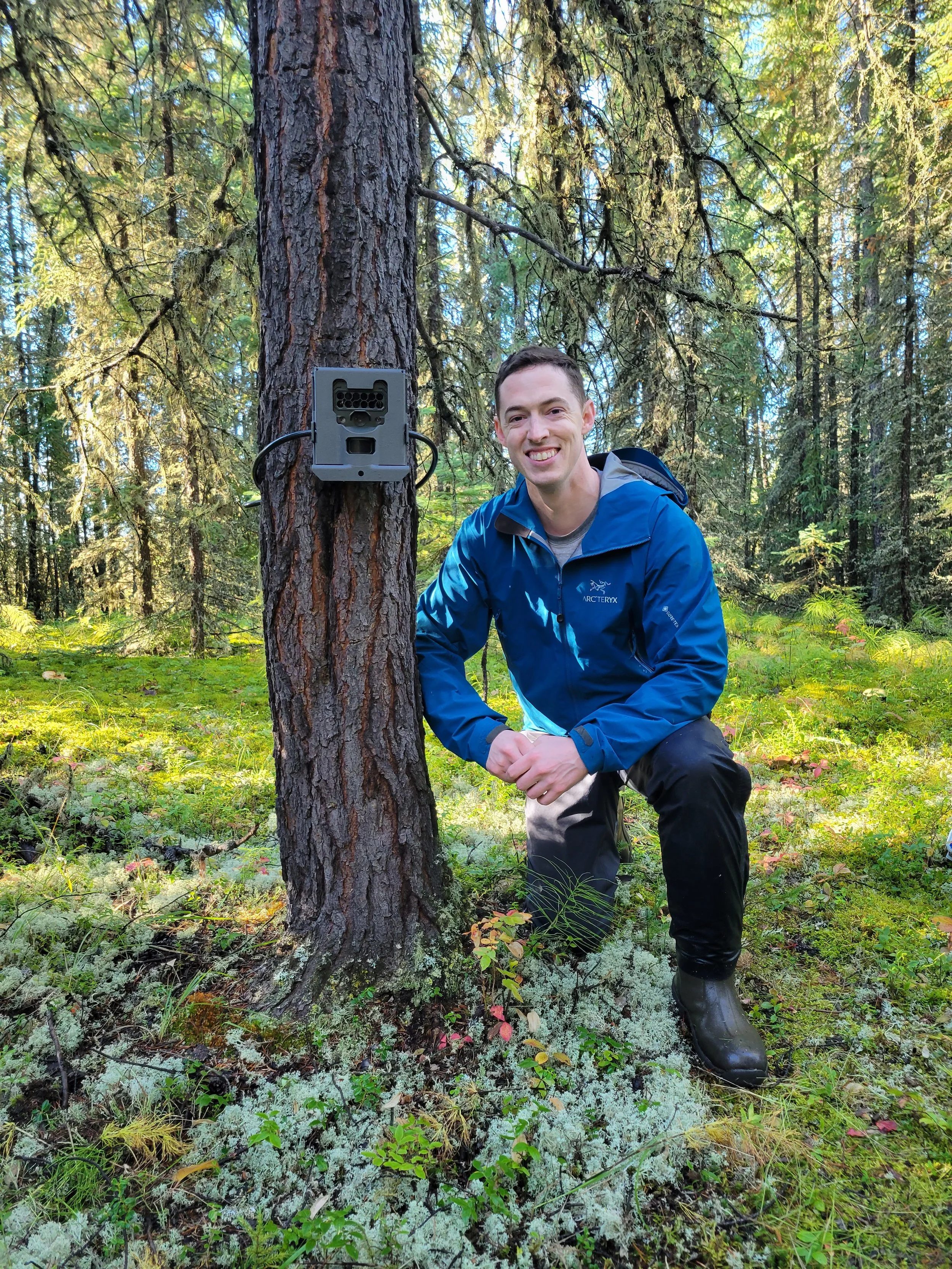 Andrew Barnas next to a remote trail camera