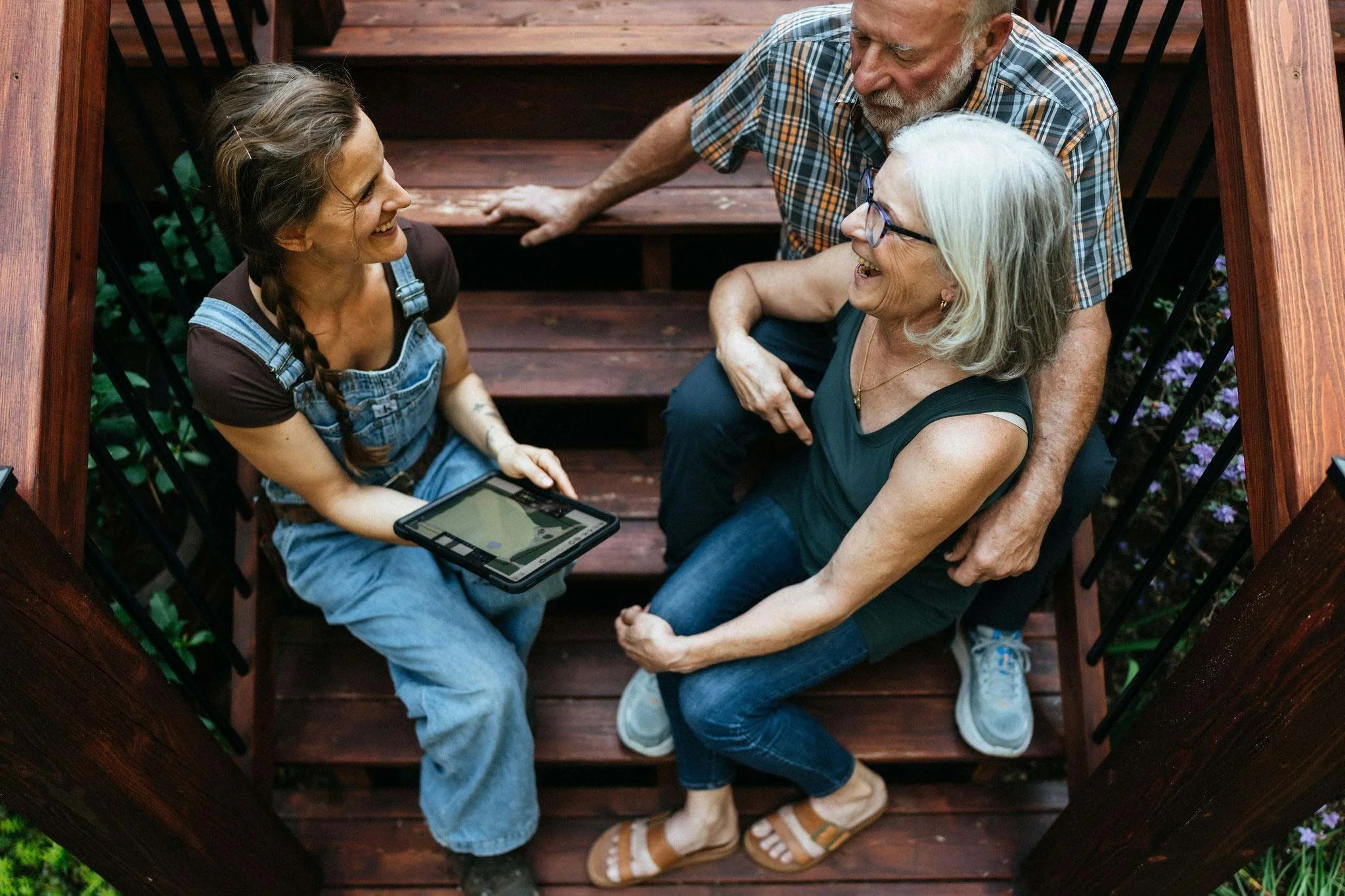 Alex sharing a garden design plan on a tablet with clients on their deck during a garden consultation on Vancouver Island