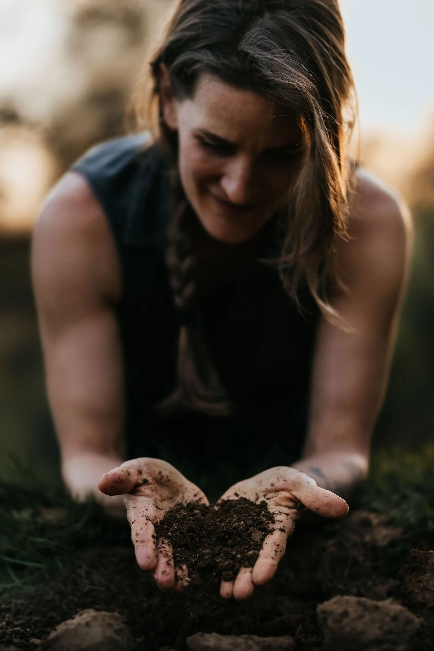 Alex, horticulture technician and founder of Plants Become Art, smiling while cradling a handful of dark garden soil