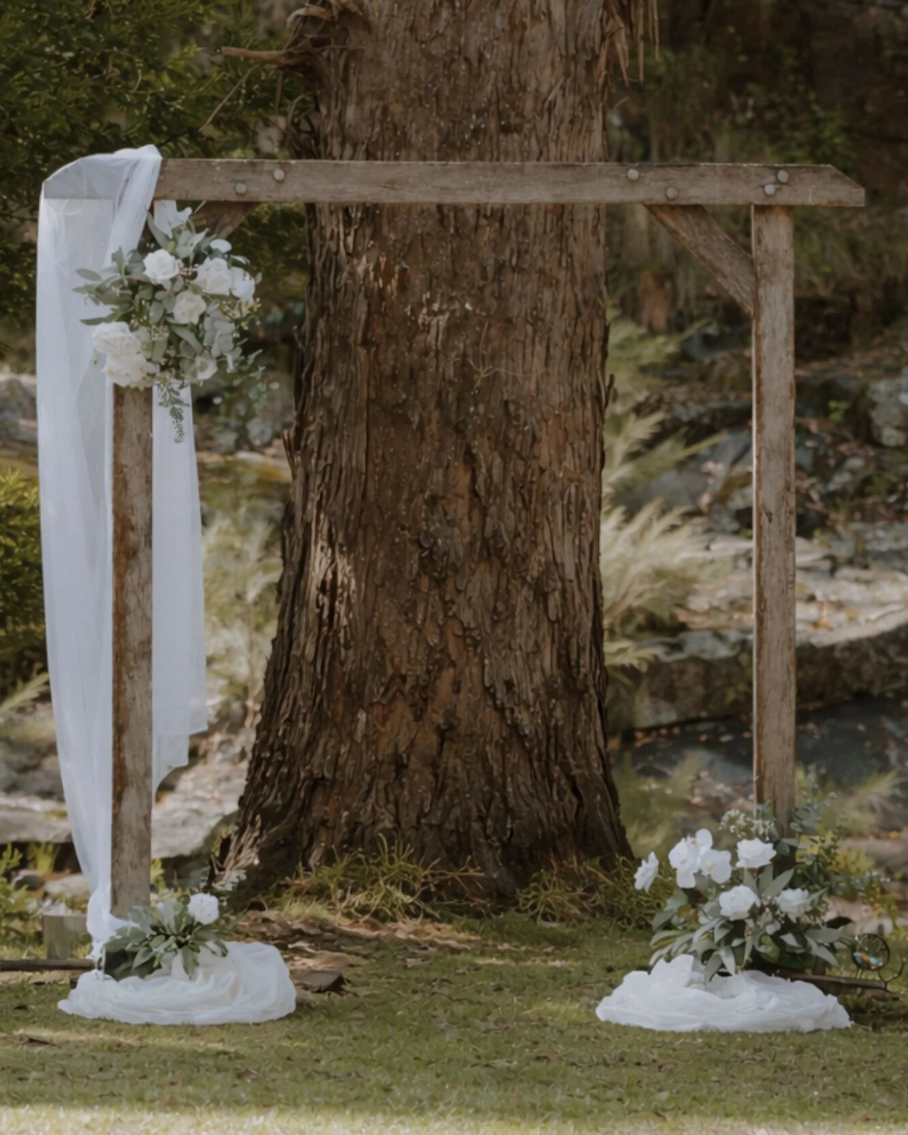 Garden wedding ceremony setup in Gold Coast with rustic timber arbour and white draped floral styling by Saudade Events.