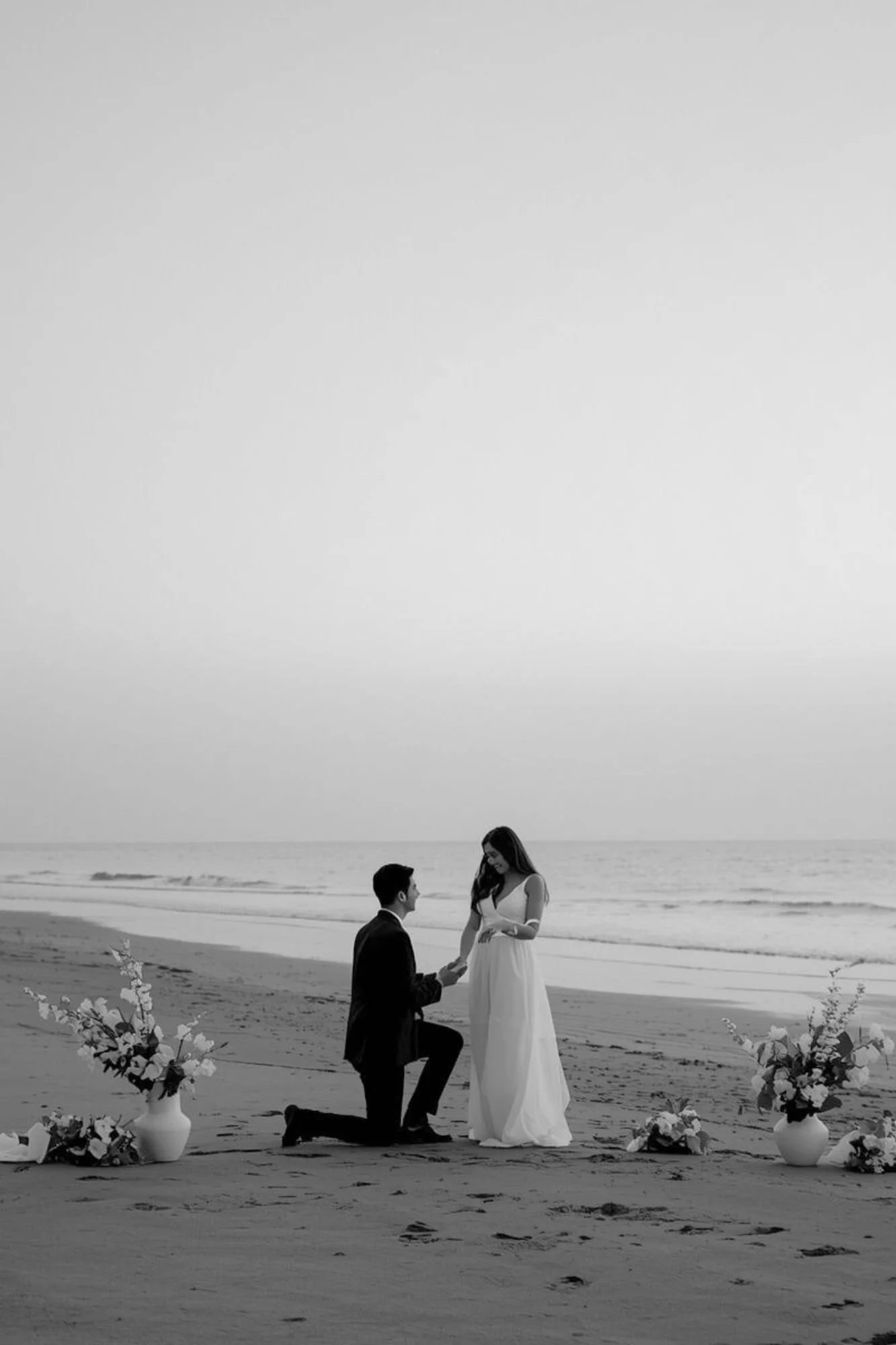 Beach proposal styling with white florals and couple during an engagement moment on the Gold Coast by Saudade Events.