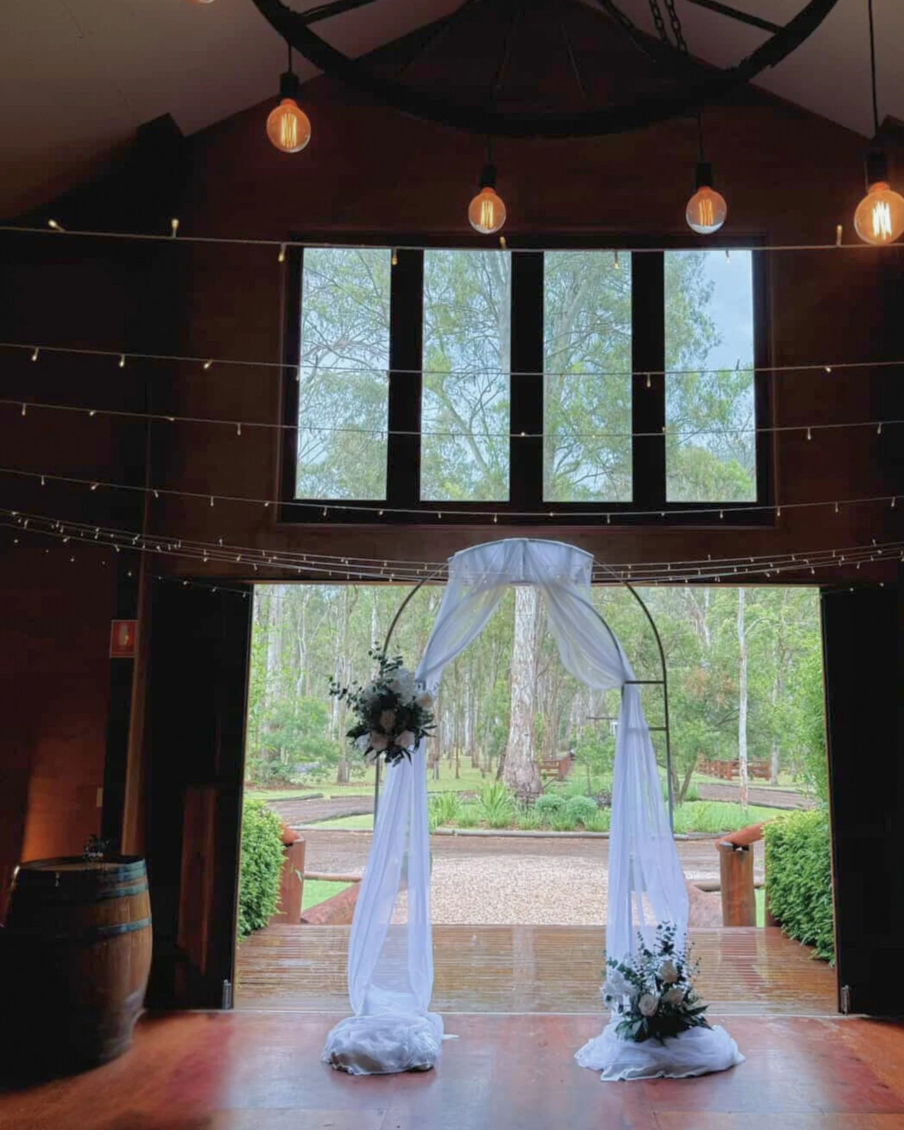 Indoor wedding ceremony setup in Gold Coast featuring white draped arbour and refined floral styling by Saudade Events.