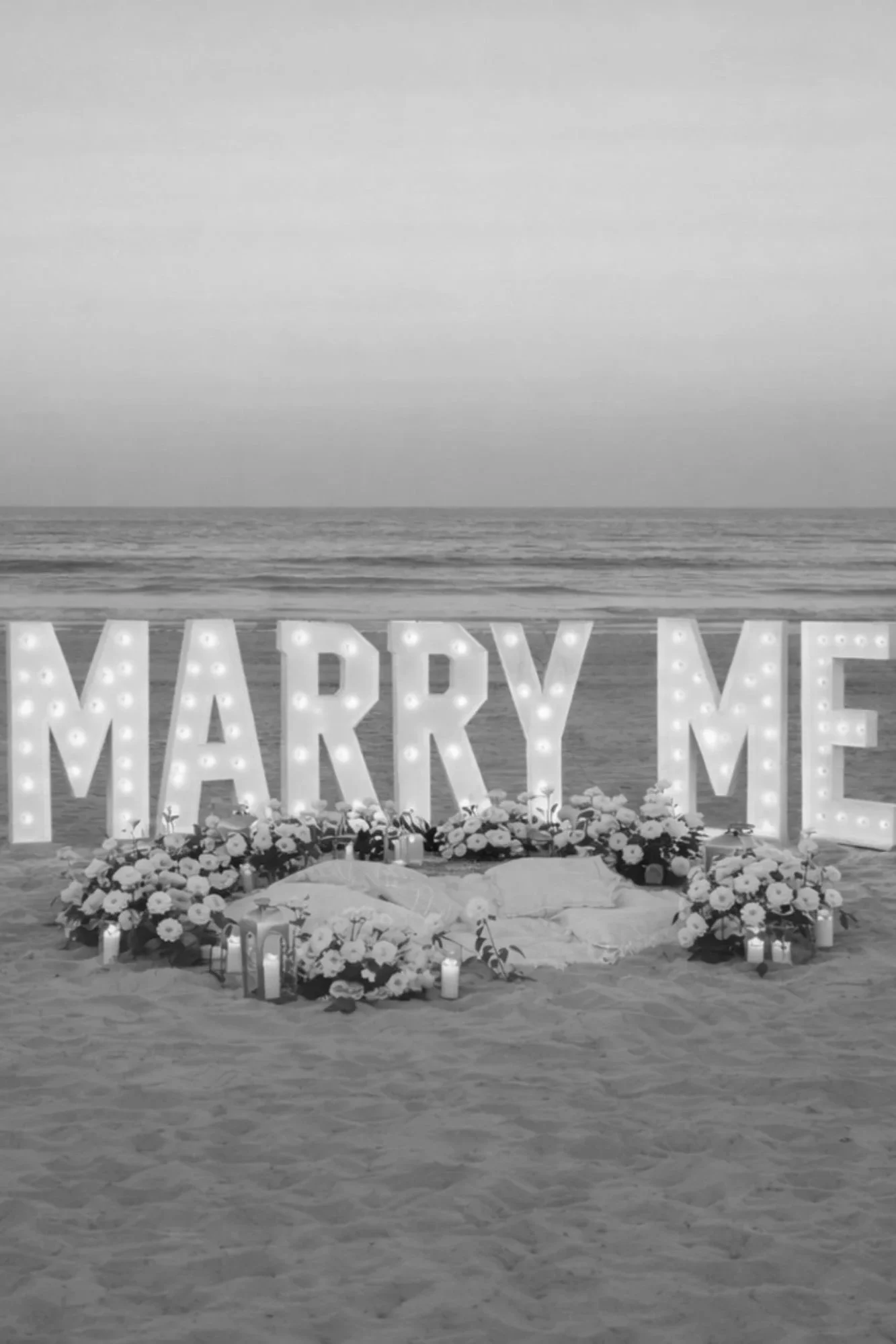 Romantic Gold Coast beach proposal setup with illuminated “Marry Me” letters, florals and candles styled by Saudade Events.