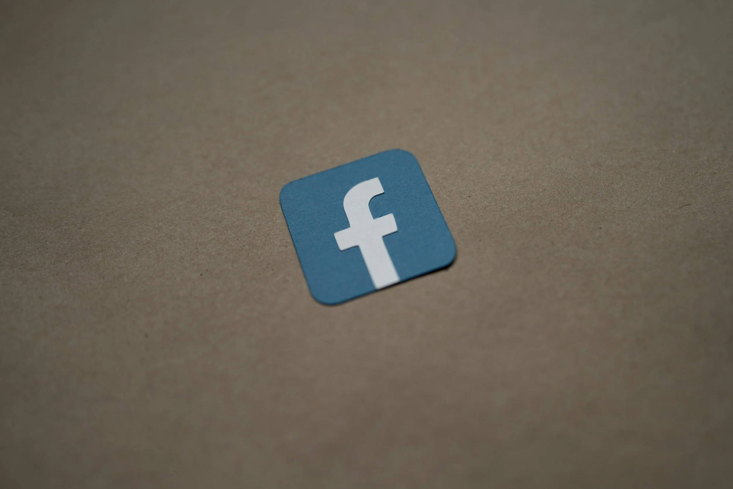 Close-up of a Facebook app icon sticker on a brown surface.