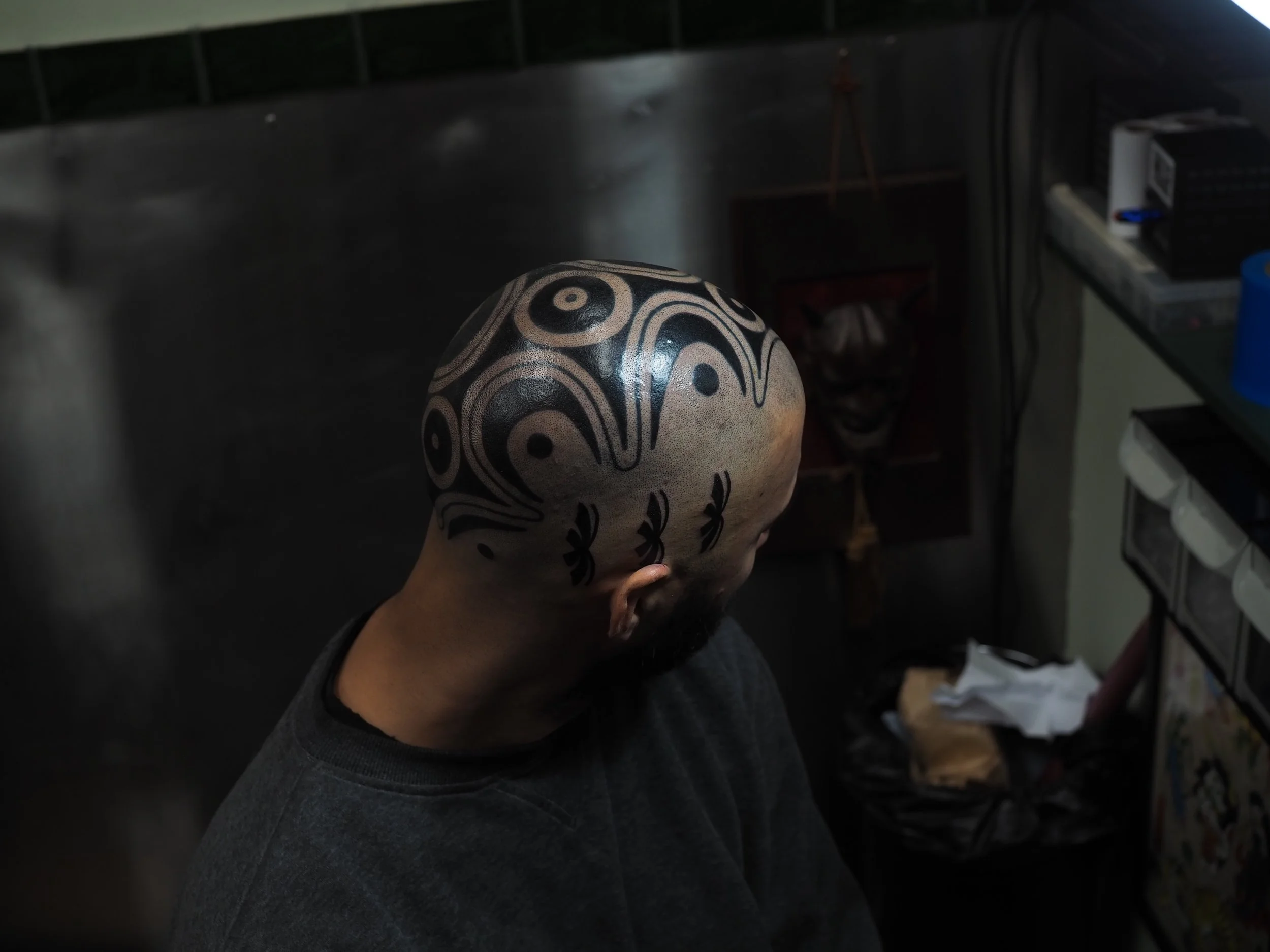 A man with tribal head tattoo on his bald head, sitting in a dimly lit room.