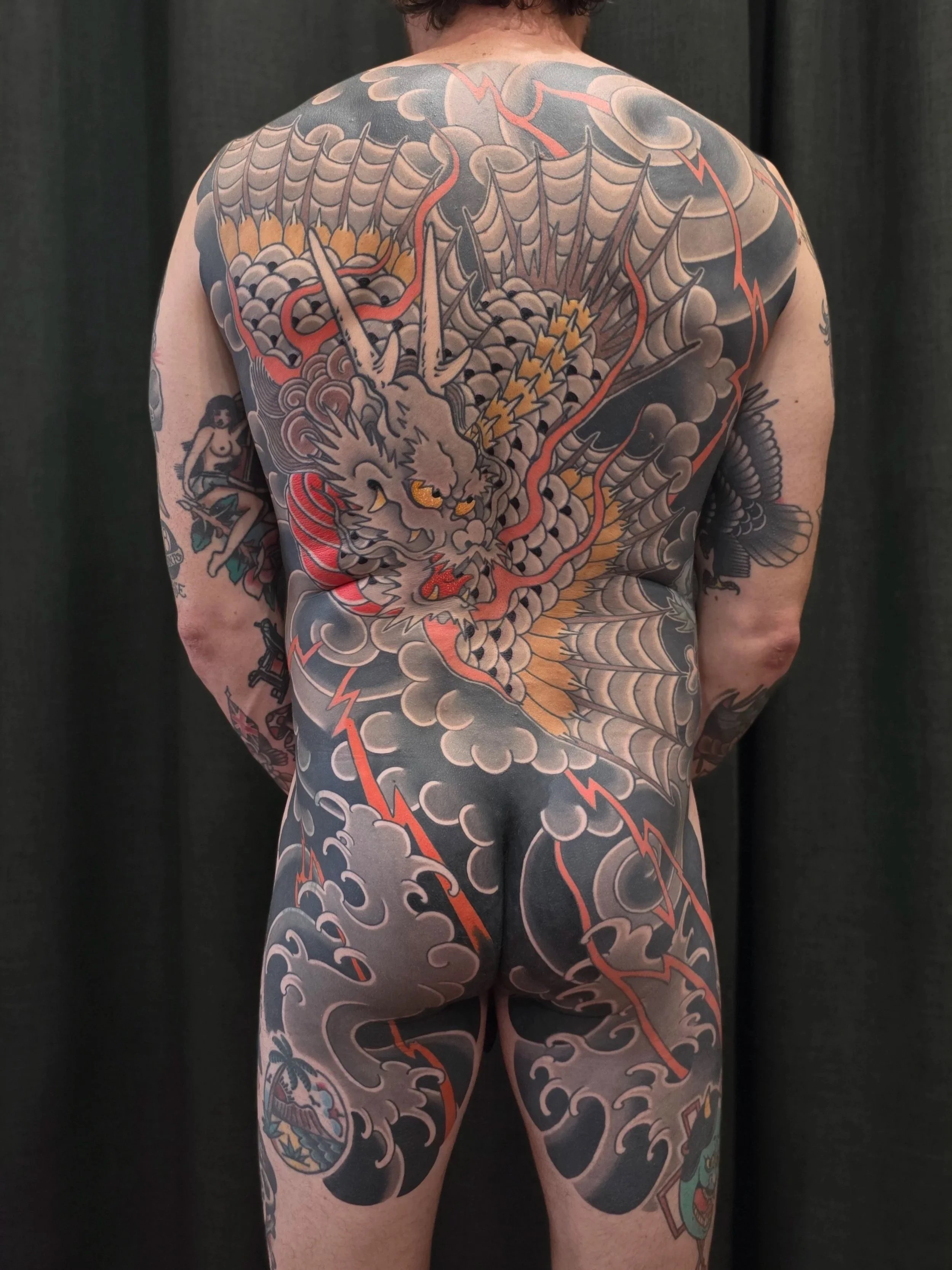 Full-back tattoo of a traditional Japanese dragon, with clouds and lightning, covering the person's back, buttocks, and thighs.