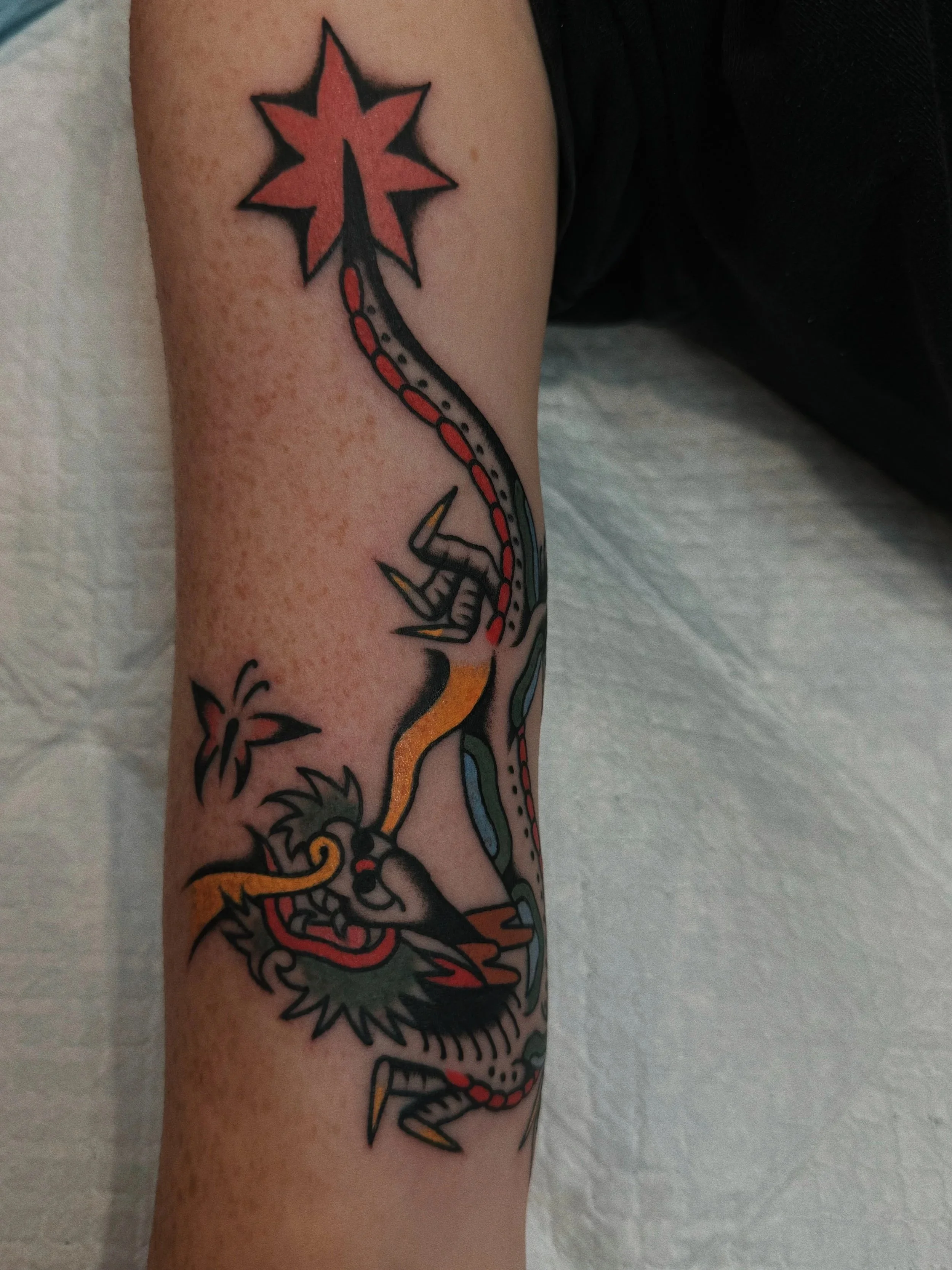 Tattoo of a traditional-style dragon with a long, winding body, horns, and sharp claws, accompanied by a butterfly and a star on the person's arm.