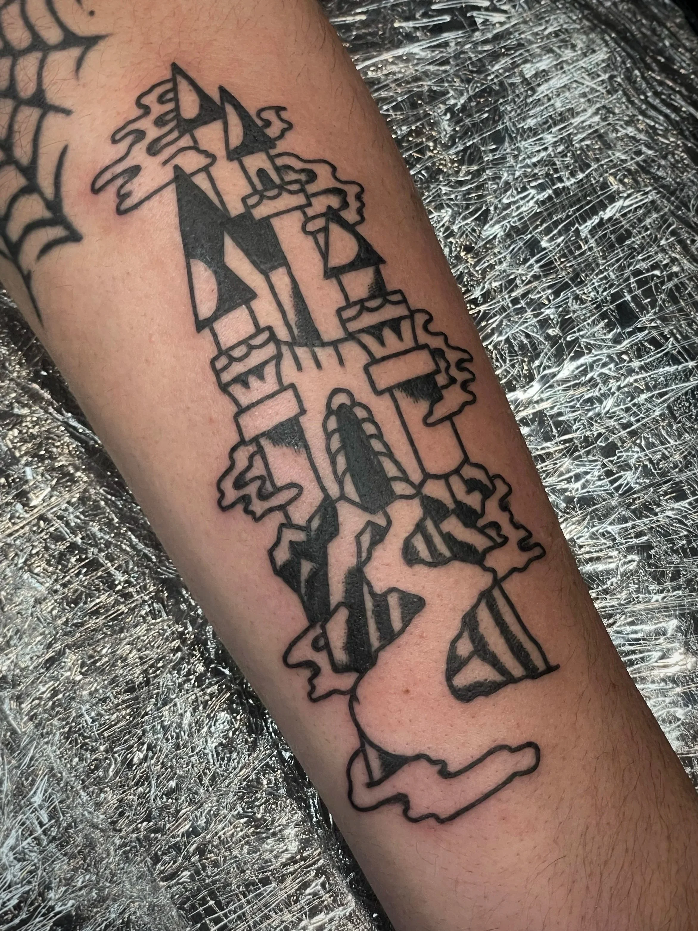 Outline tattoo of a castle with  towers, windows, and a central door, depicted on a person's forearm.