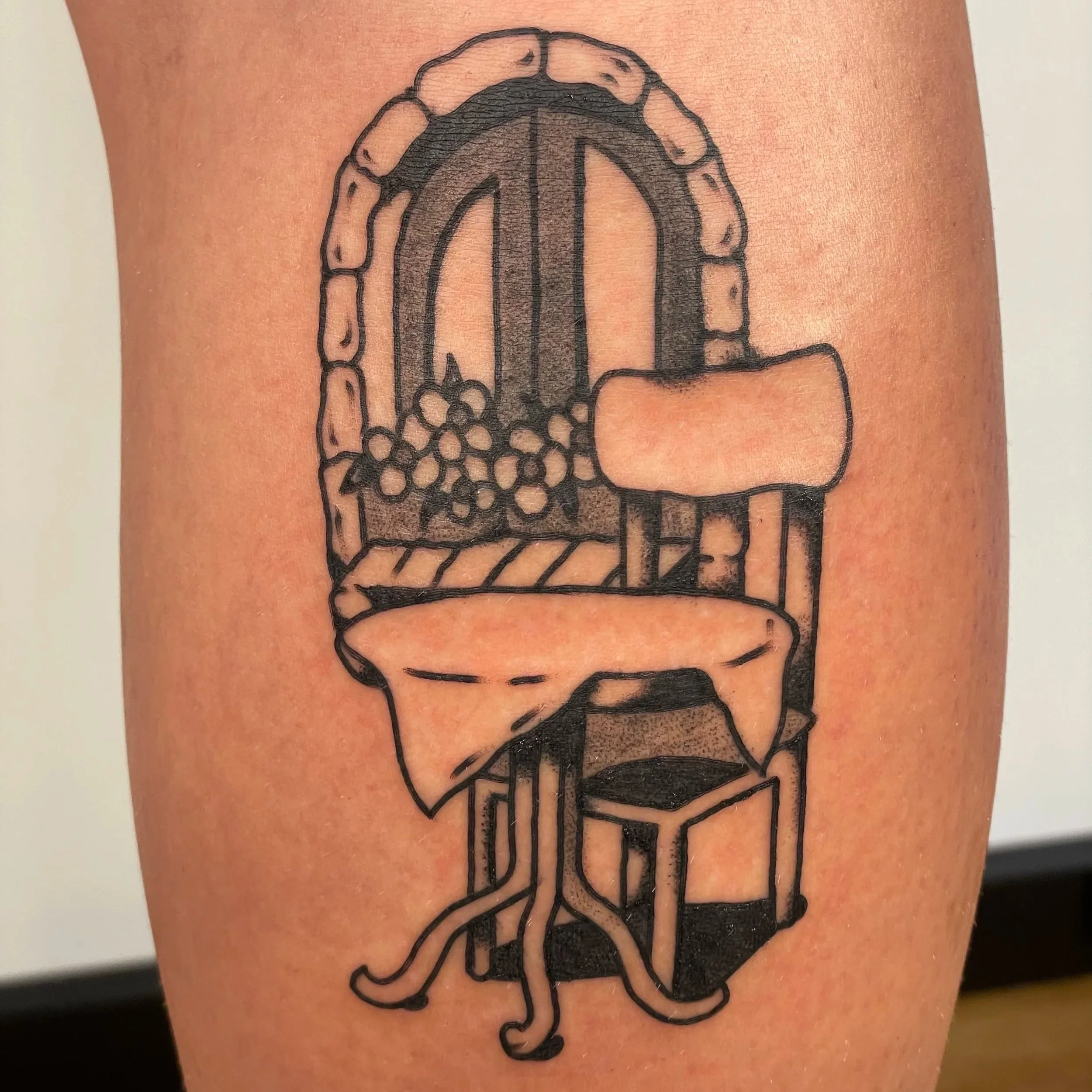 Tattoo of a wooden chair with a tablecloth on the seat, placed in front of a window with a flower box and curtains.