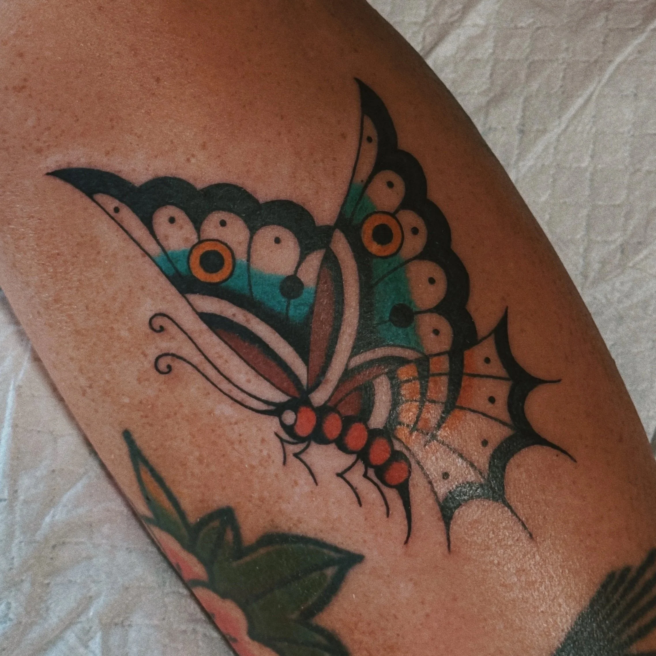 Colorful butterfly tattoo with black, orange, teal, and pink details on skin.