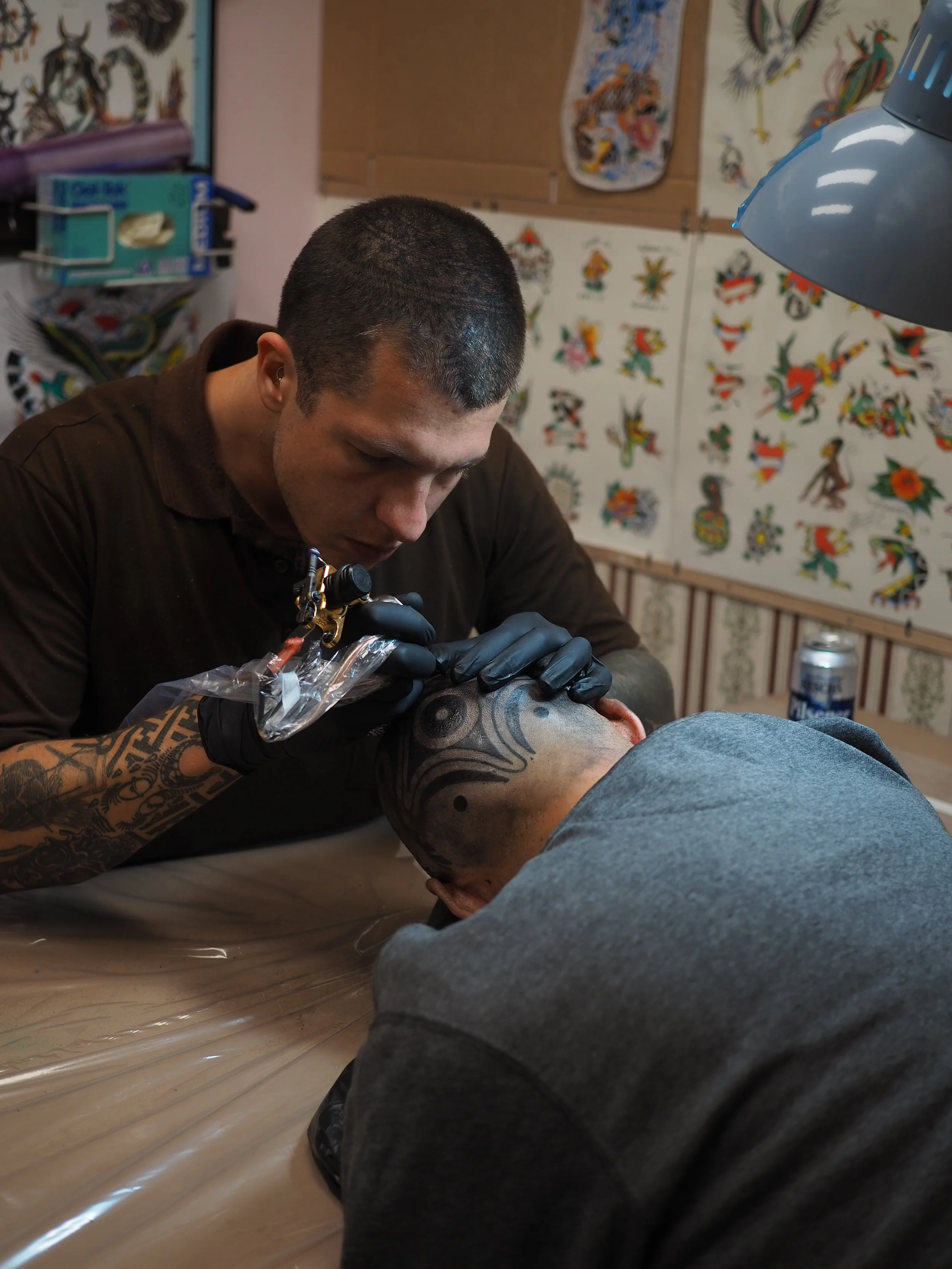 Tattoo artist tattooing a man's head with tribal designs in a tattoo shop.