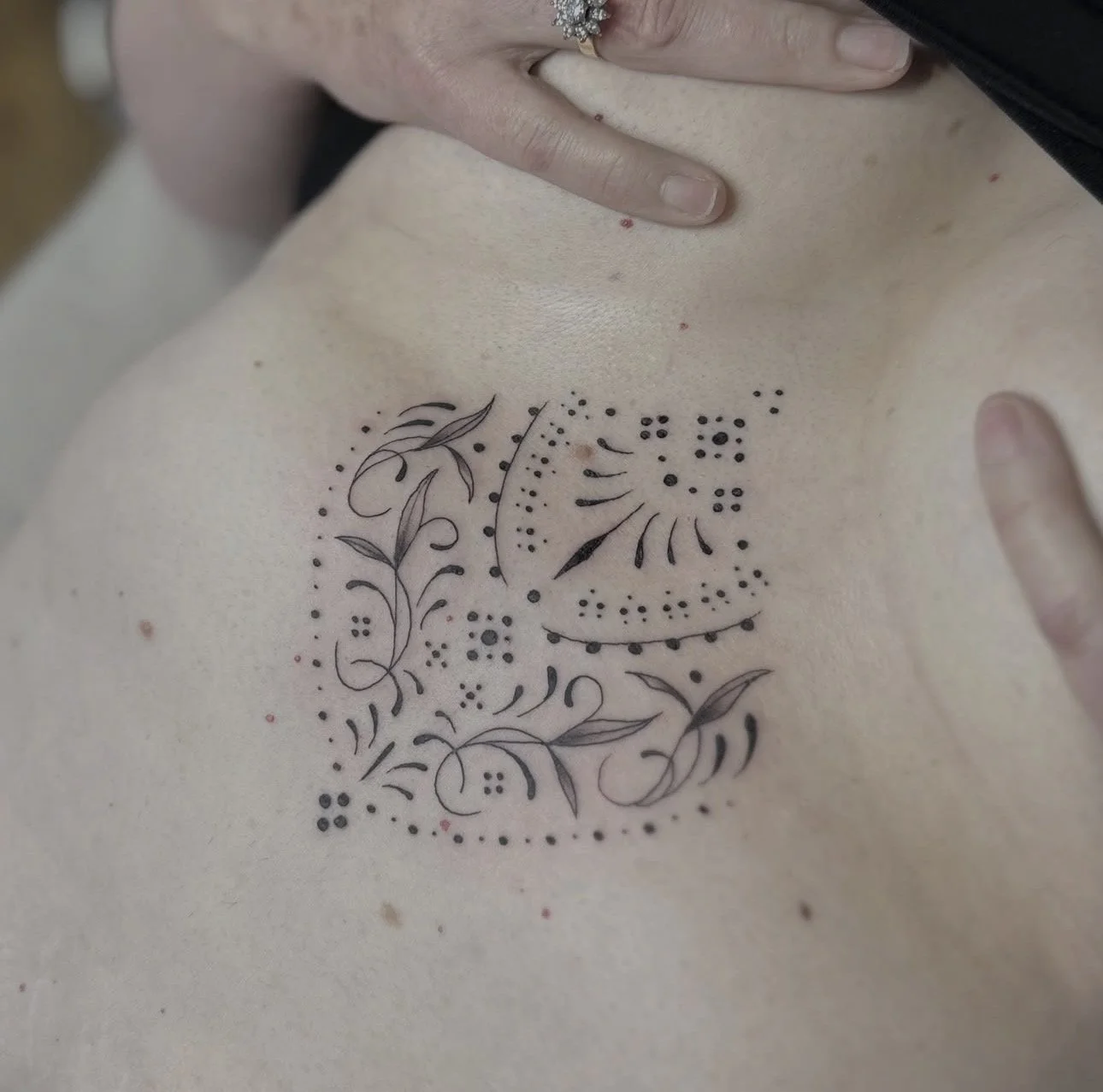 A person's chest with a newly tattooed design featuring floral and abstract patterns in black ink.