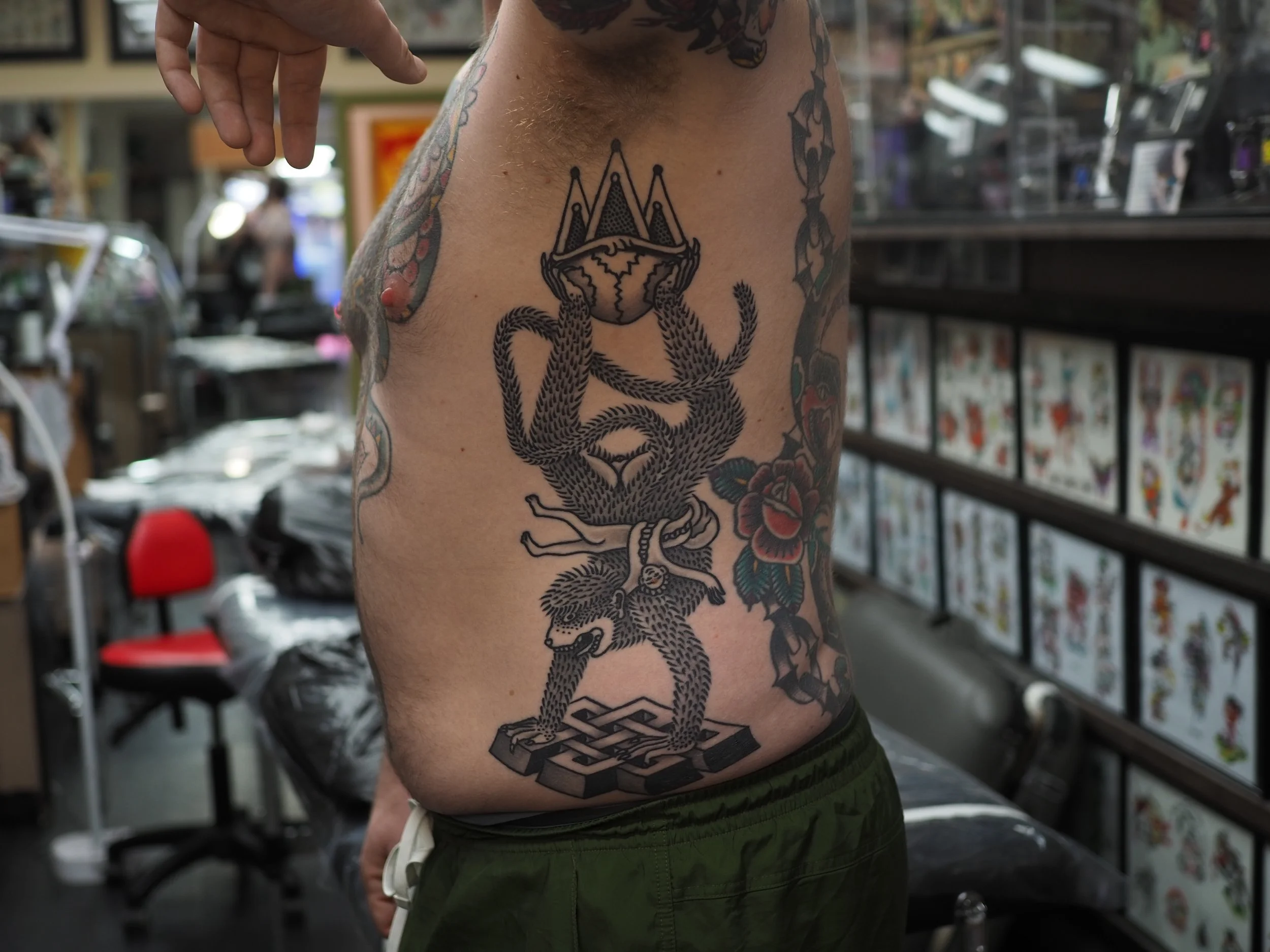 Tattoo of a monkey holding a flame on a man's side, with a floral design nearby, in a tattoo parlor.