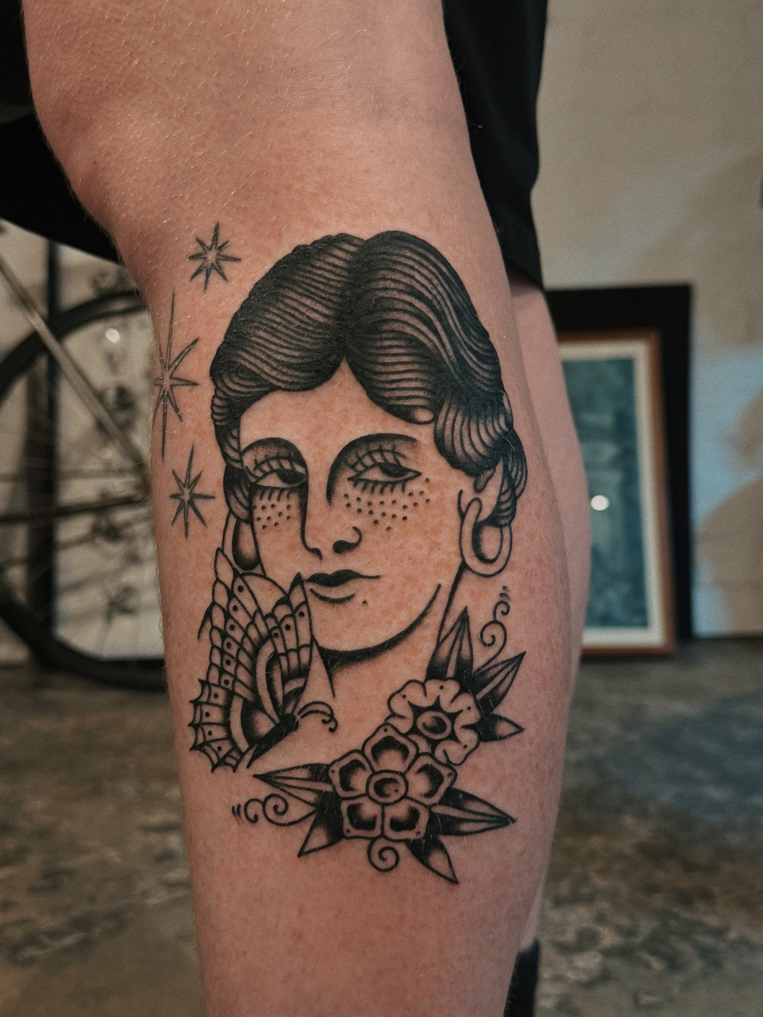 Tattoo of a woman's face with short hair, freckles, and earrings, surrounded by stars, a butterfly near her face, and flowers at her neck.