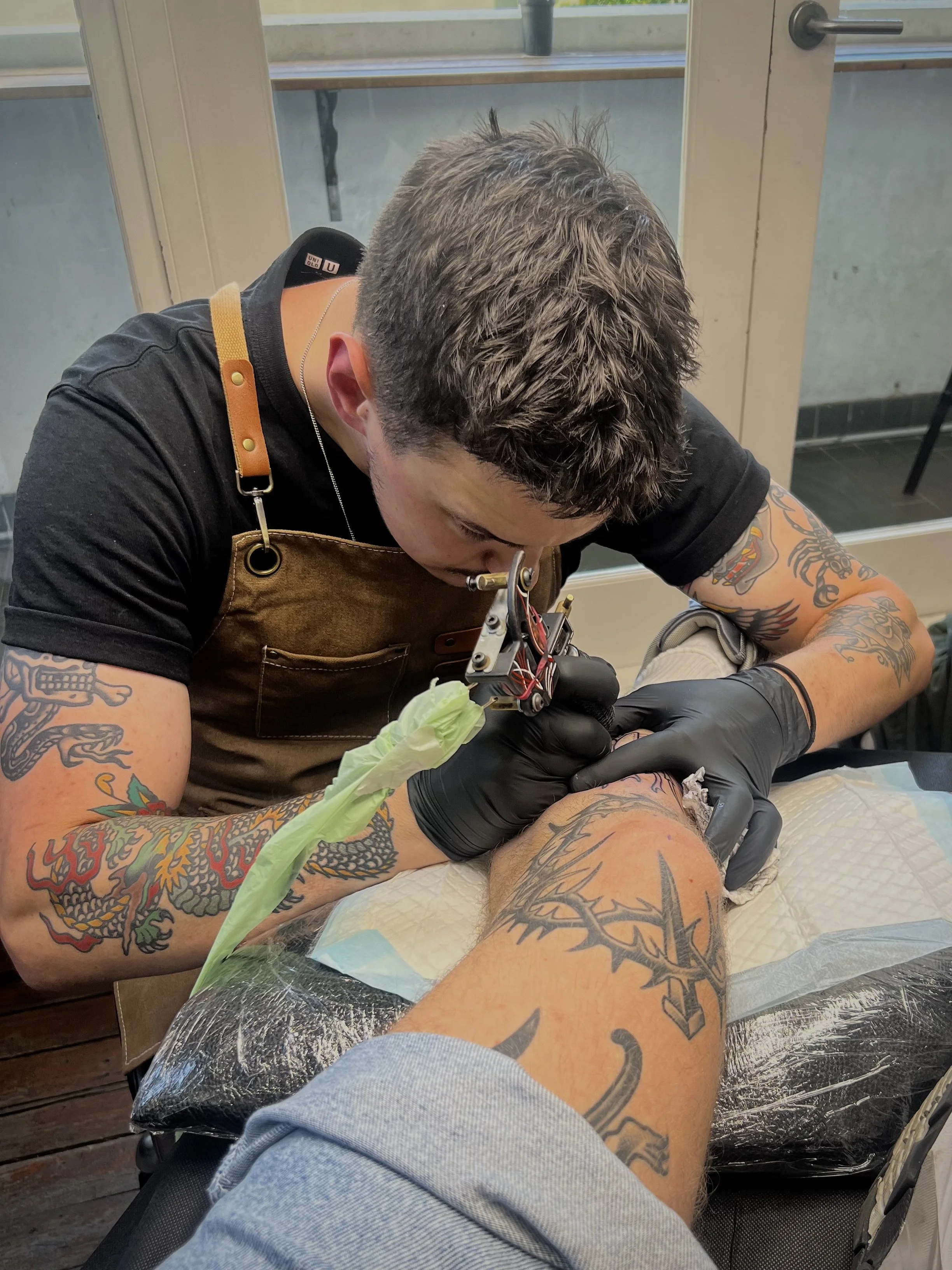 Tattoo artist working on a client's leg in a tattoo studio.
